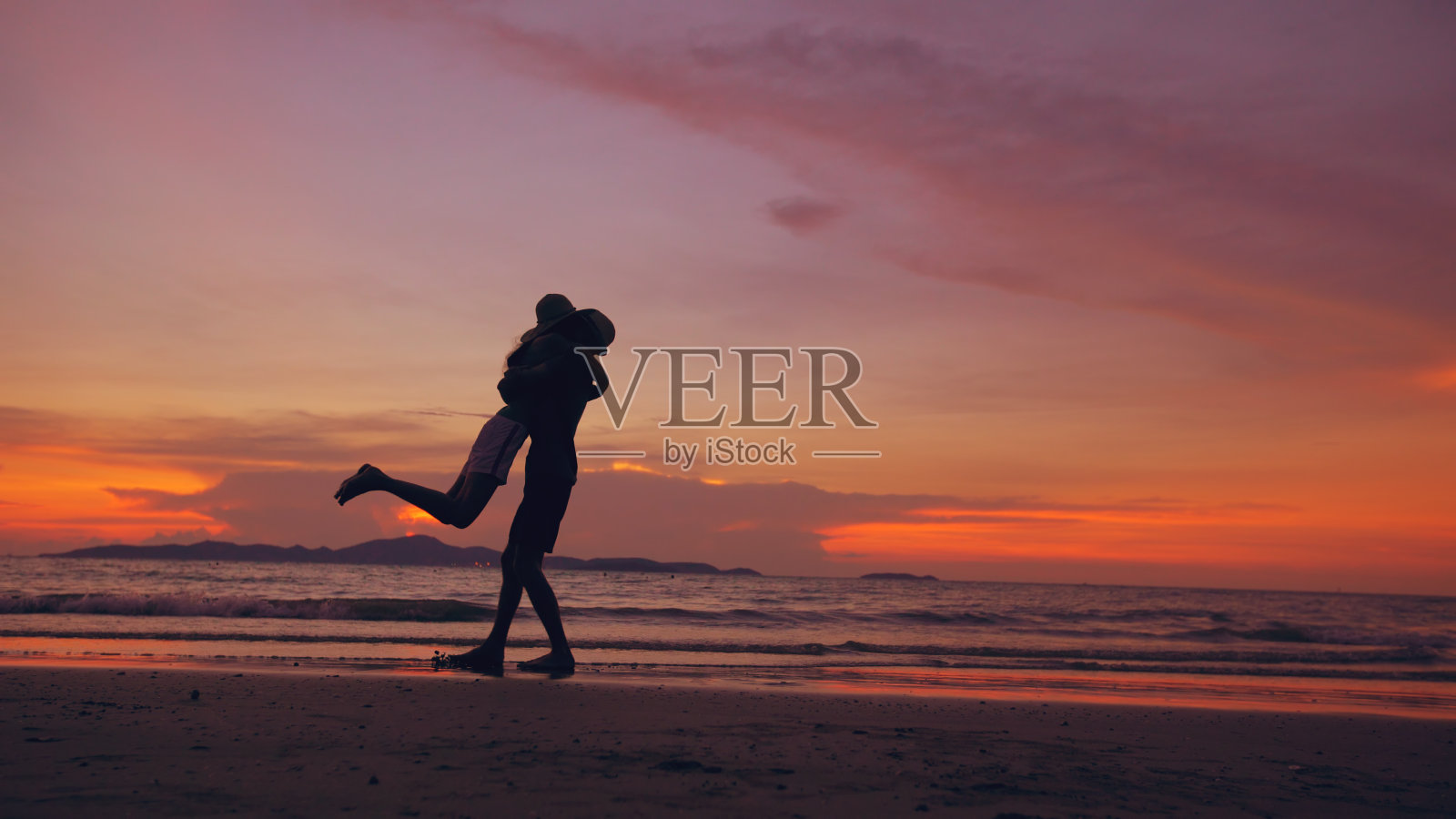 一对幸福的情侣的剪影相遇，在海边的日落沙滩上玩耍照片摄影图片