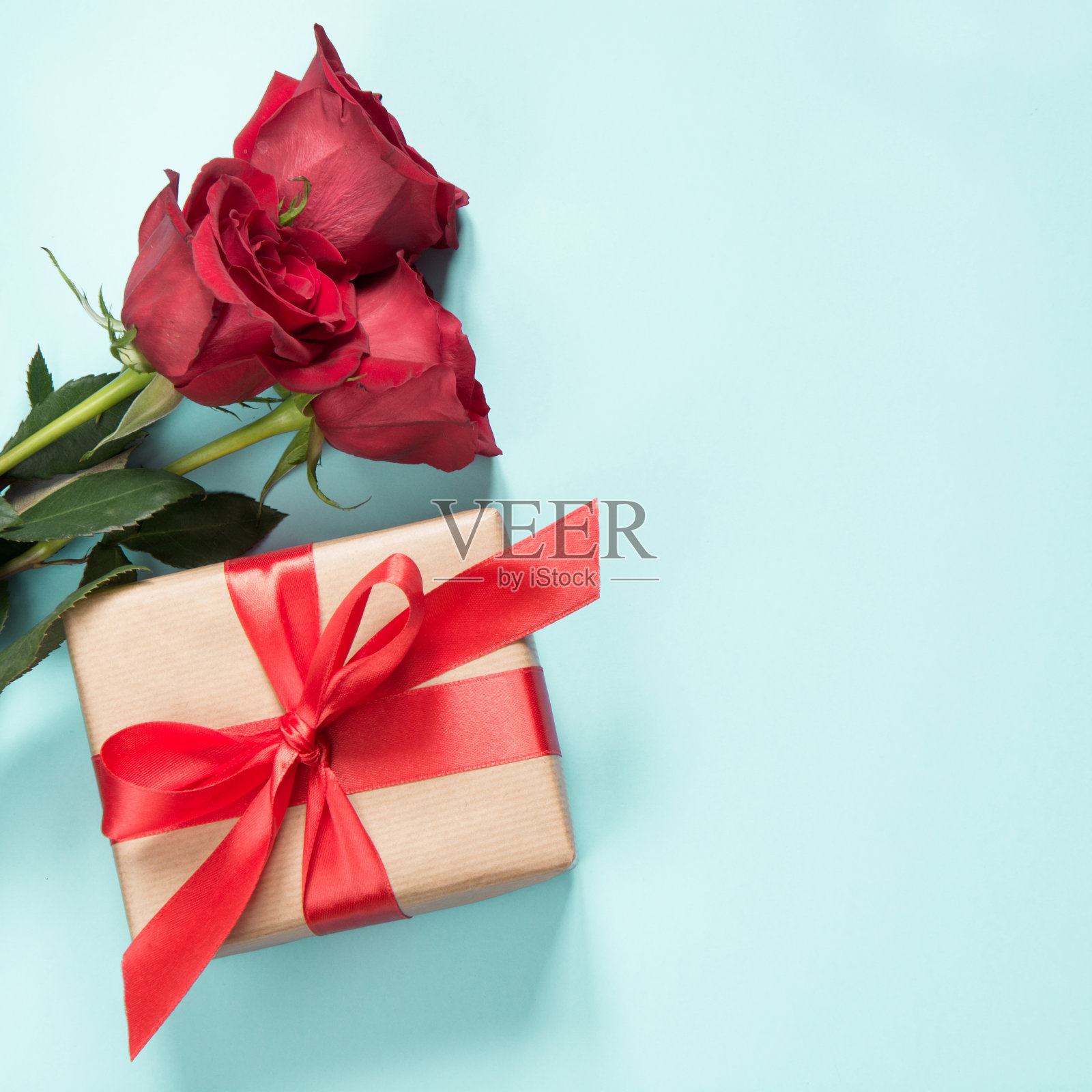 一束红玫瑰和一份以淡蓝色为背景的红丝带礼物。情人节卡片。关闭了。副本的空间。照片摄影图片
