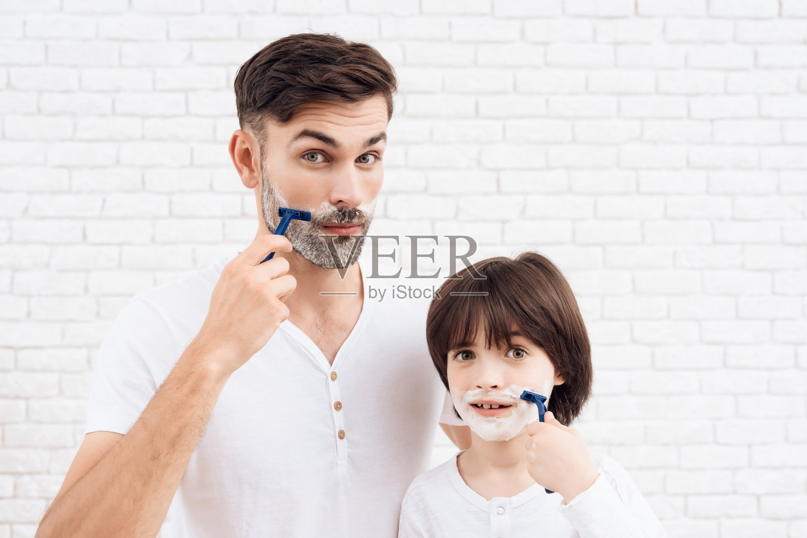 父亲和儿子花时间在一起。爸爸和儿子穿着一样的衣服。那个黑头发的小男孩学会了刮胡子。照片摄影图片