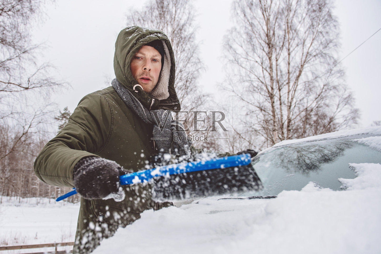 在寒冷的冬天，一名男子正在清除他汽车上的积雪照片摄影图片