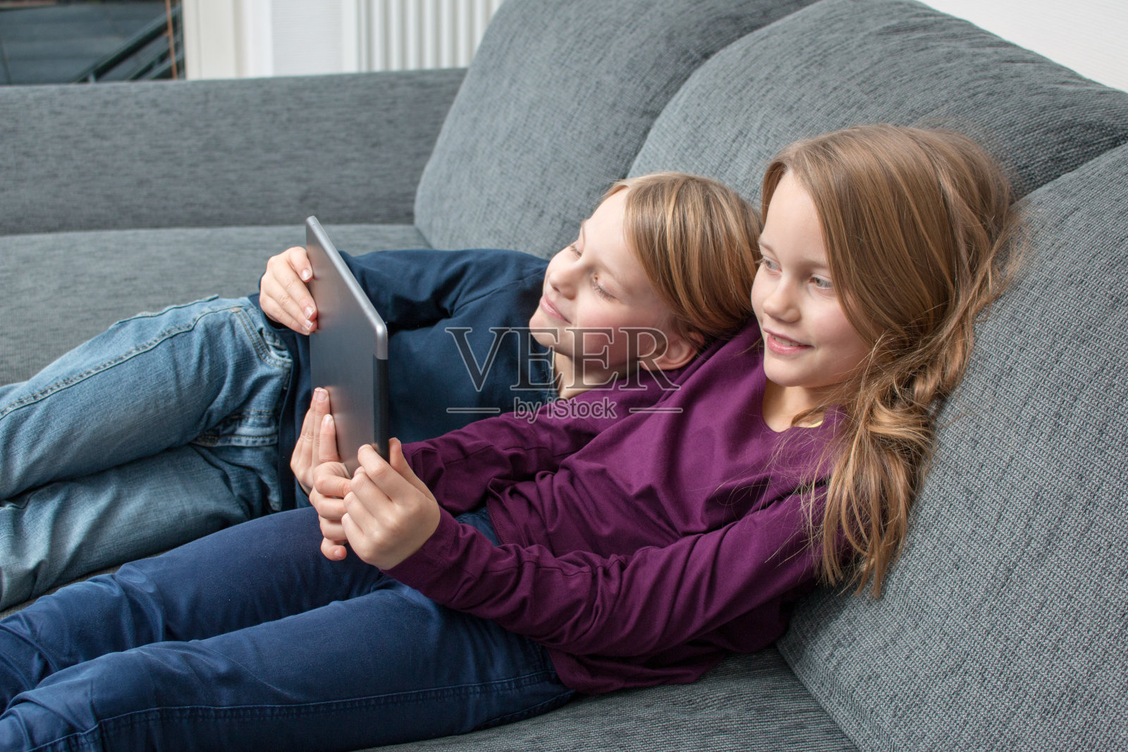 两个女孩在沙发上放松，用平板电脑娱乐照片摄影图片