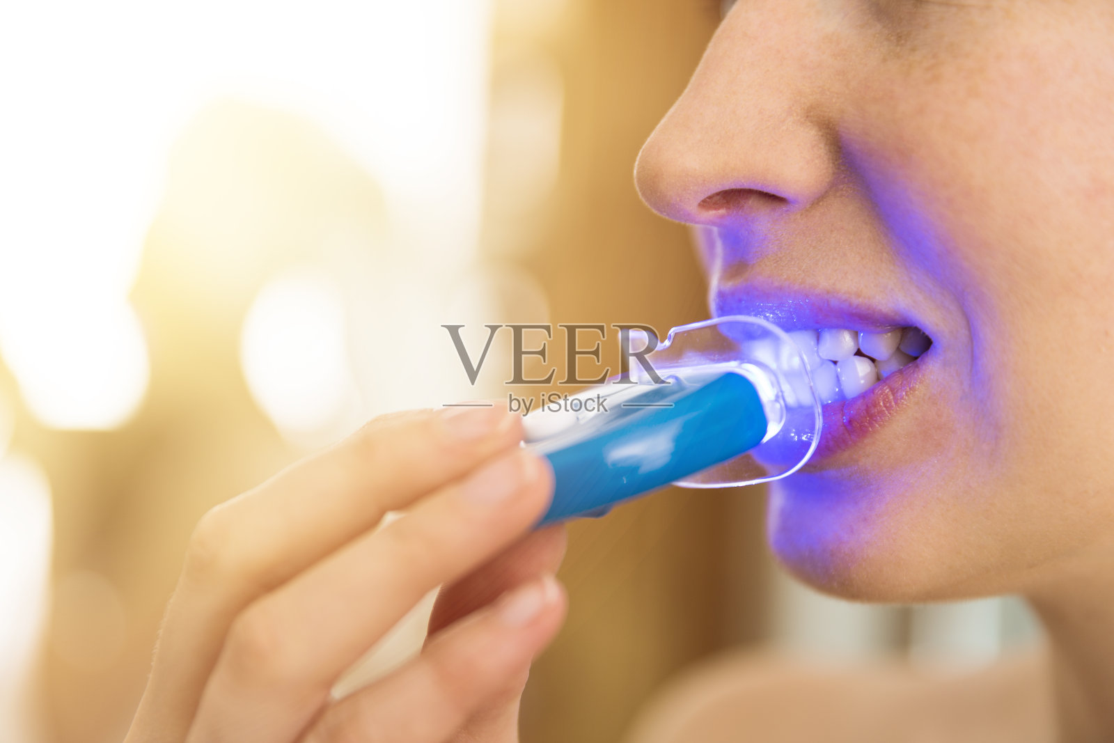 一个女人在家里用特殊的牙膏和LED灯美白牙齿。美丽的概念照片摄影图片