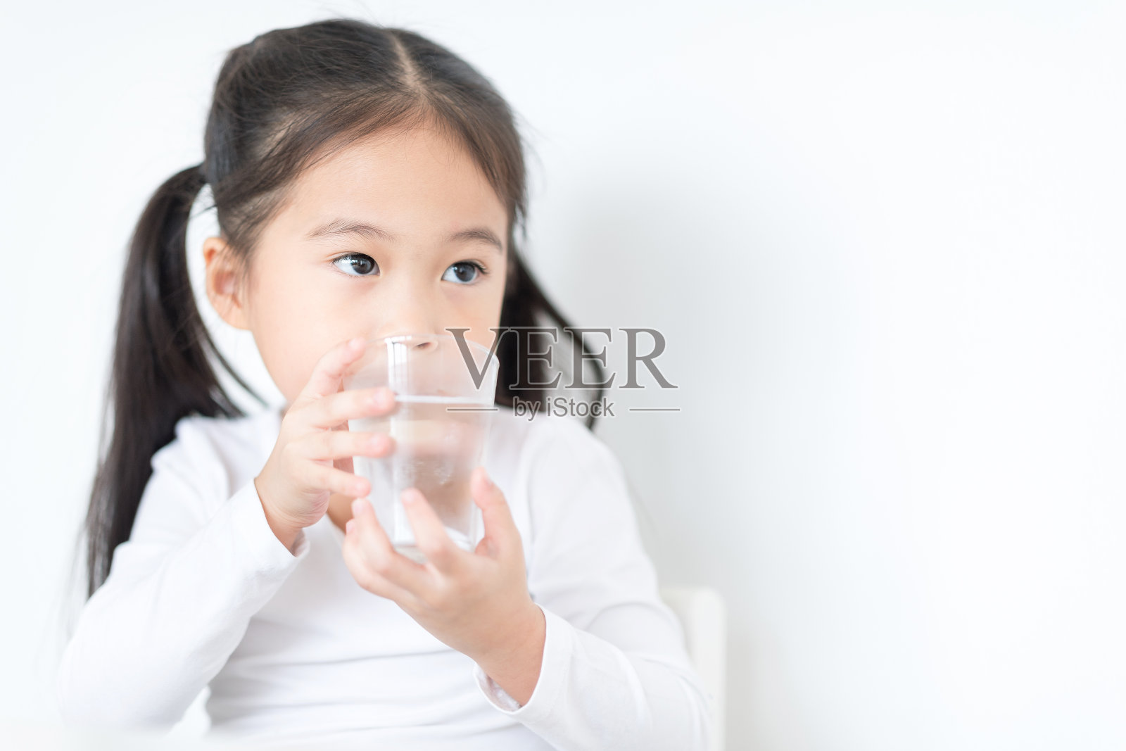 漂亮的女孩正在喝着一杯水，看着外面。照片摄影图片