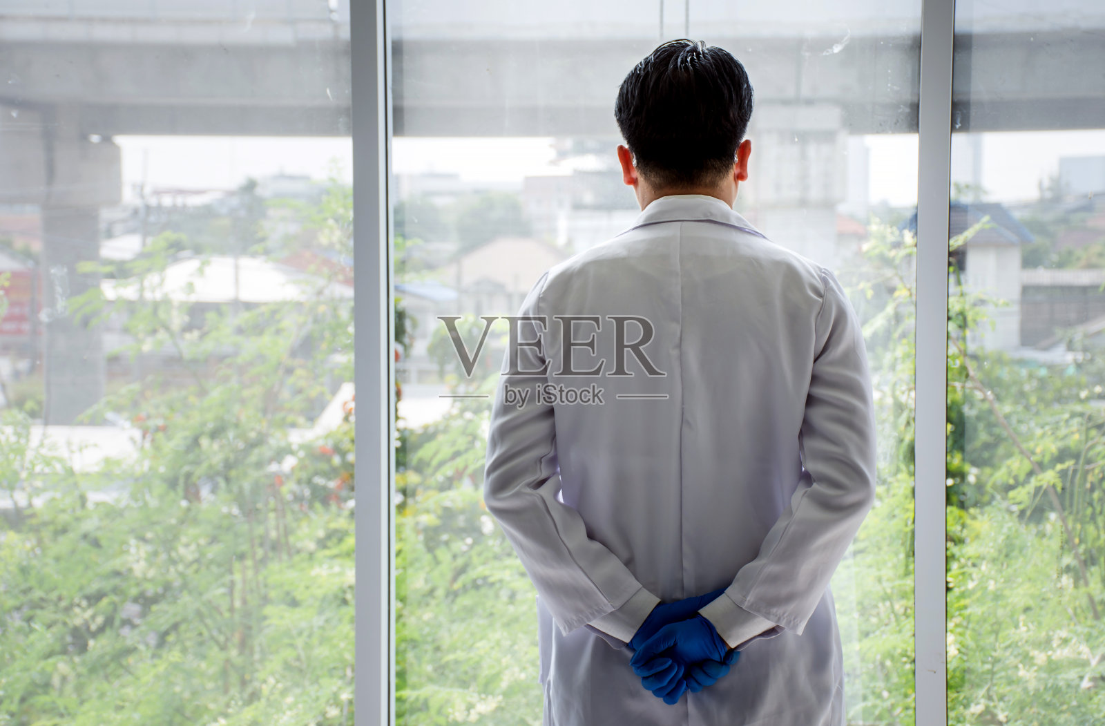 亚洲医生站在你的背后，双手紧握，看着窗外照片摄影图片
