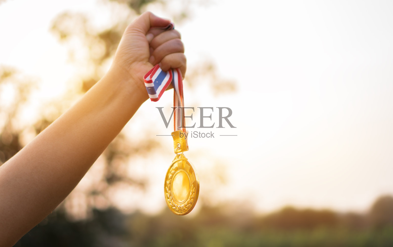 模糊的女人的手举起，拿着金牌与泰国缎带的蓝天背景显示在体育或商业上的成功，获奖者成功的奖项概念。照片摄影图片