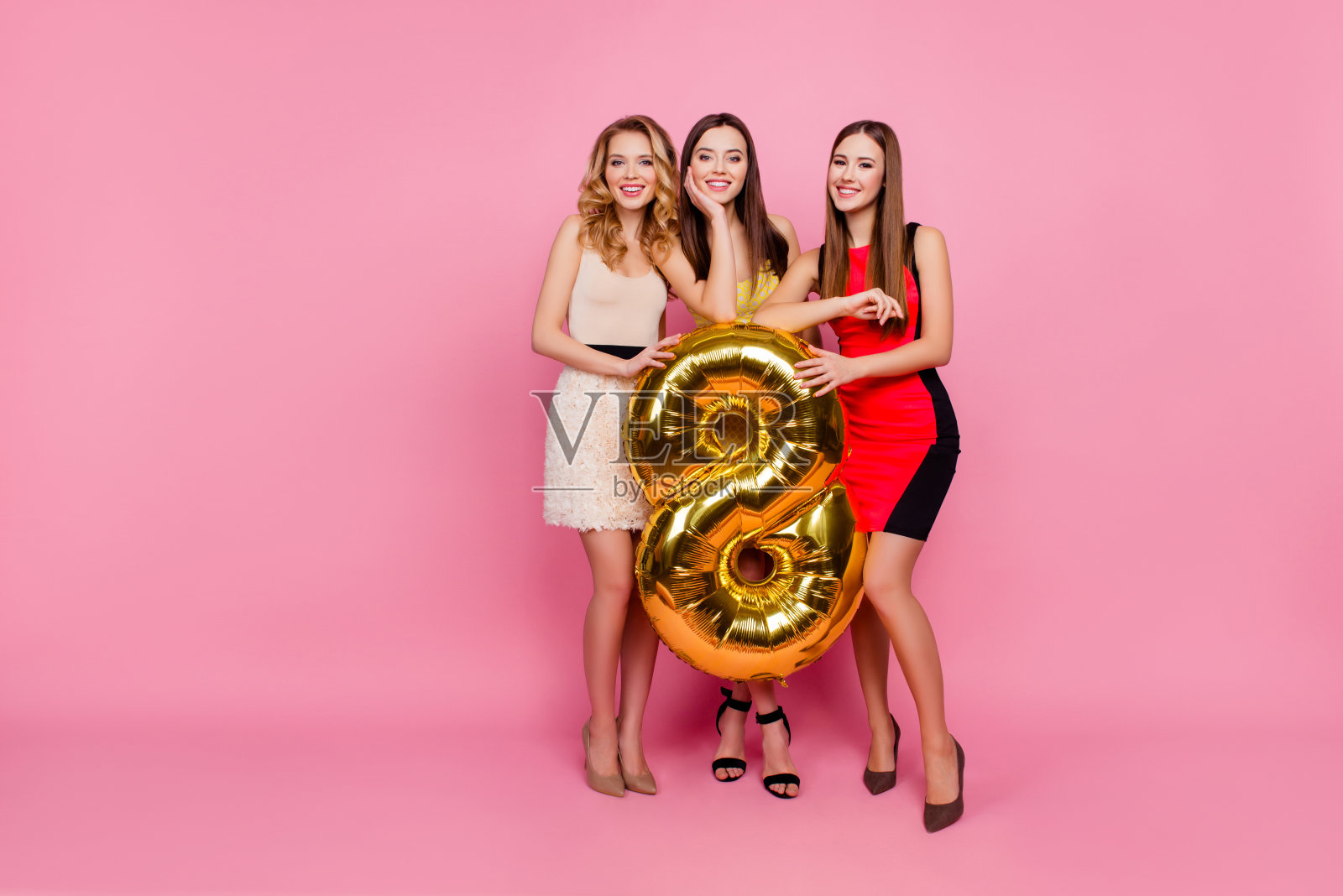 全身像的三个漂亮的女孩，派对时间时尚的女孩群在优雅的服装庆祝，妇女节，八点钟，举着金色的气球，站在粉红色的背景照片摄影图片