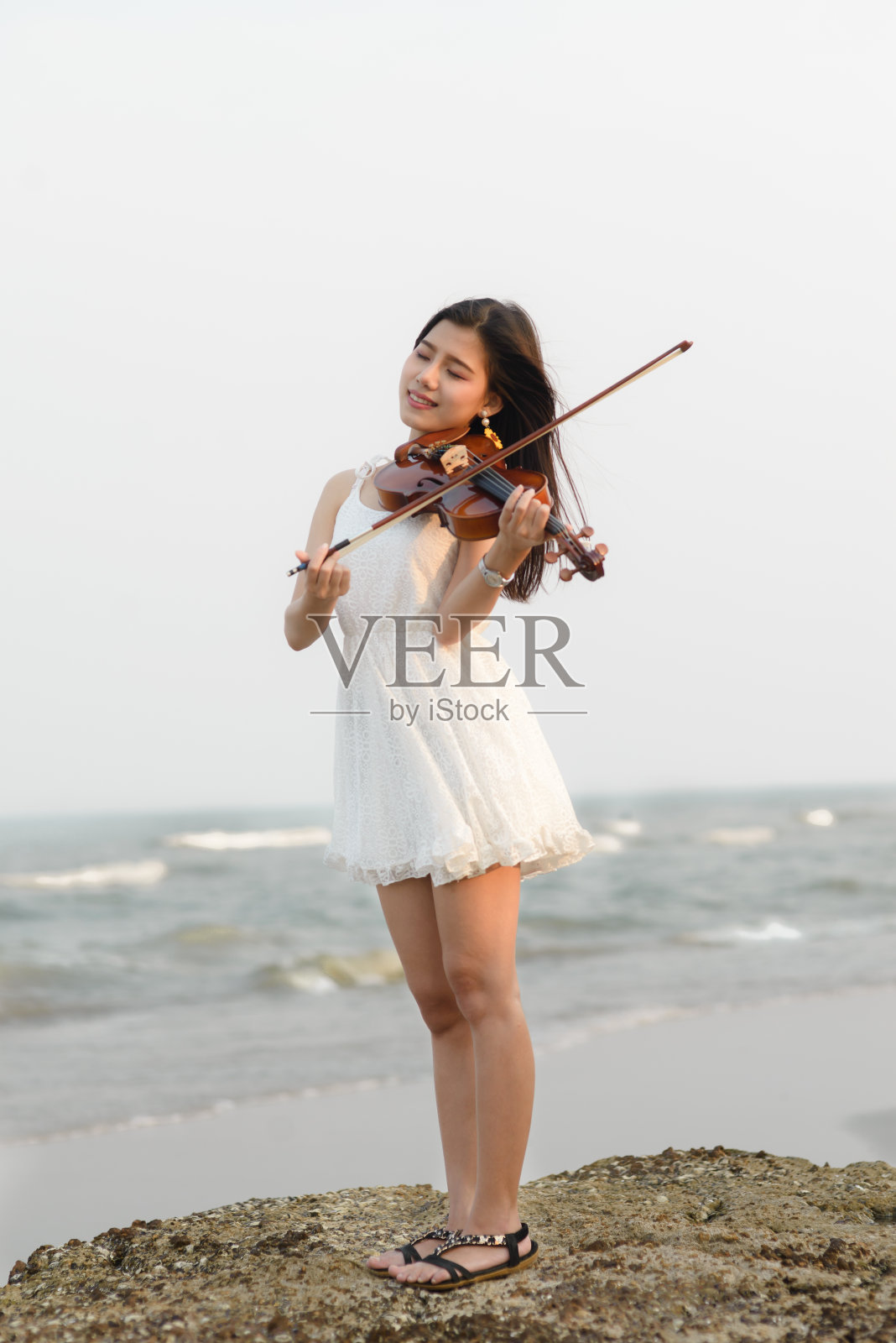 在海滩上拉小提琴的快乐女人。照片摄影图片