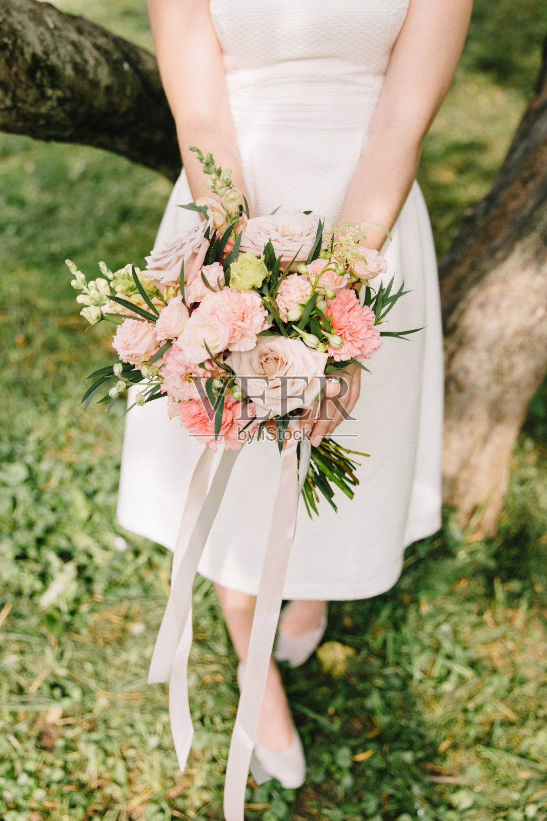新娘身穿白色礼服，手持一束以绿色花园为背景的乡村婚礼花束。夏天,户外活动。照片摄影图片