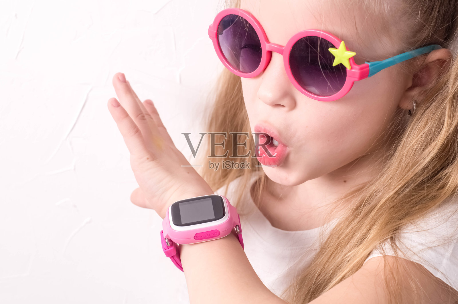 儿童科技:一个戴着粉色眼镜的女孩用着智能手表。照片摄影图片