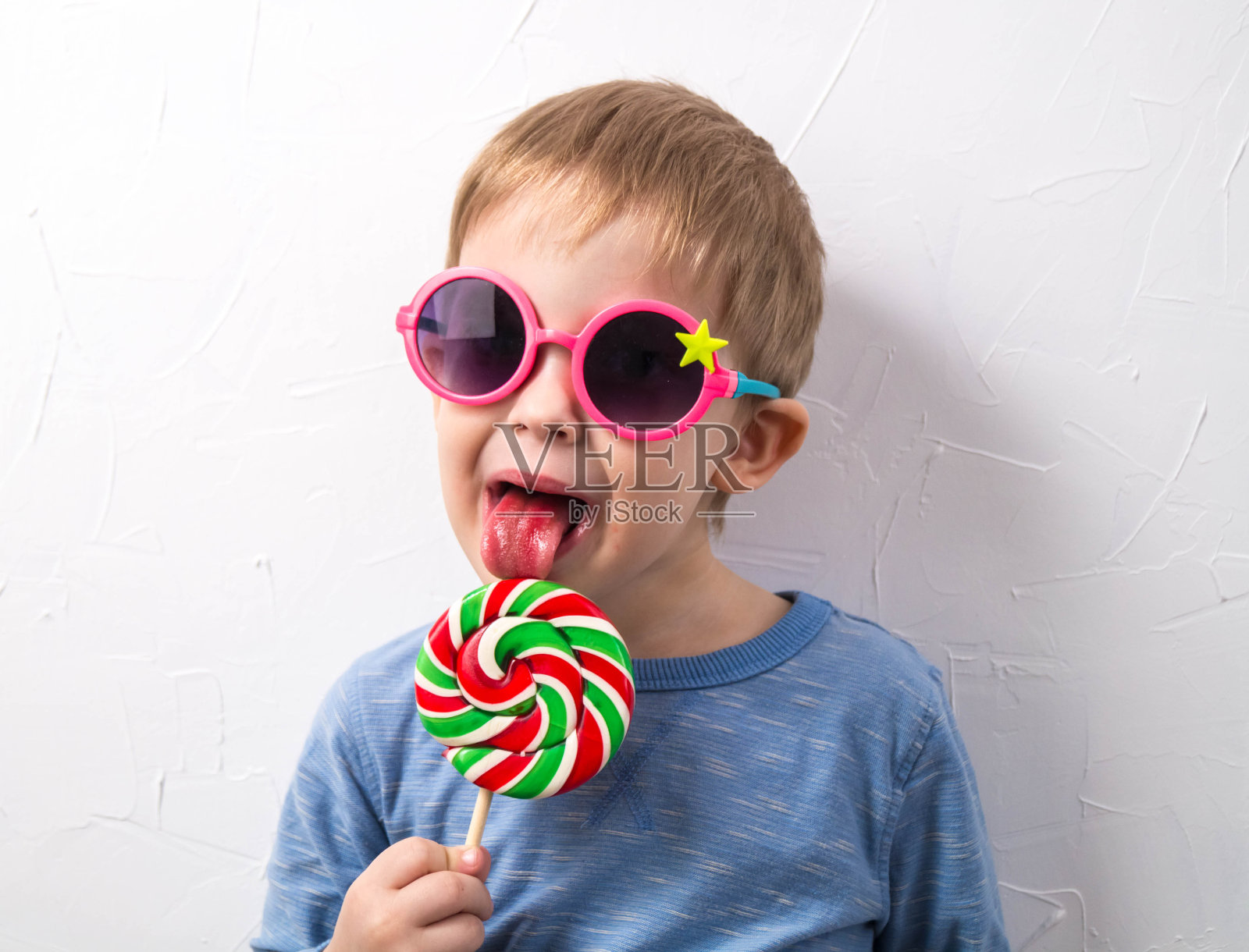 糖果和童年:一个戴着粉红色眼镜的小男孩，手里拿着一颗圆圆的糖果照片摄影图片