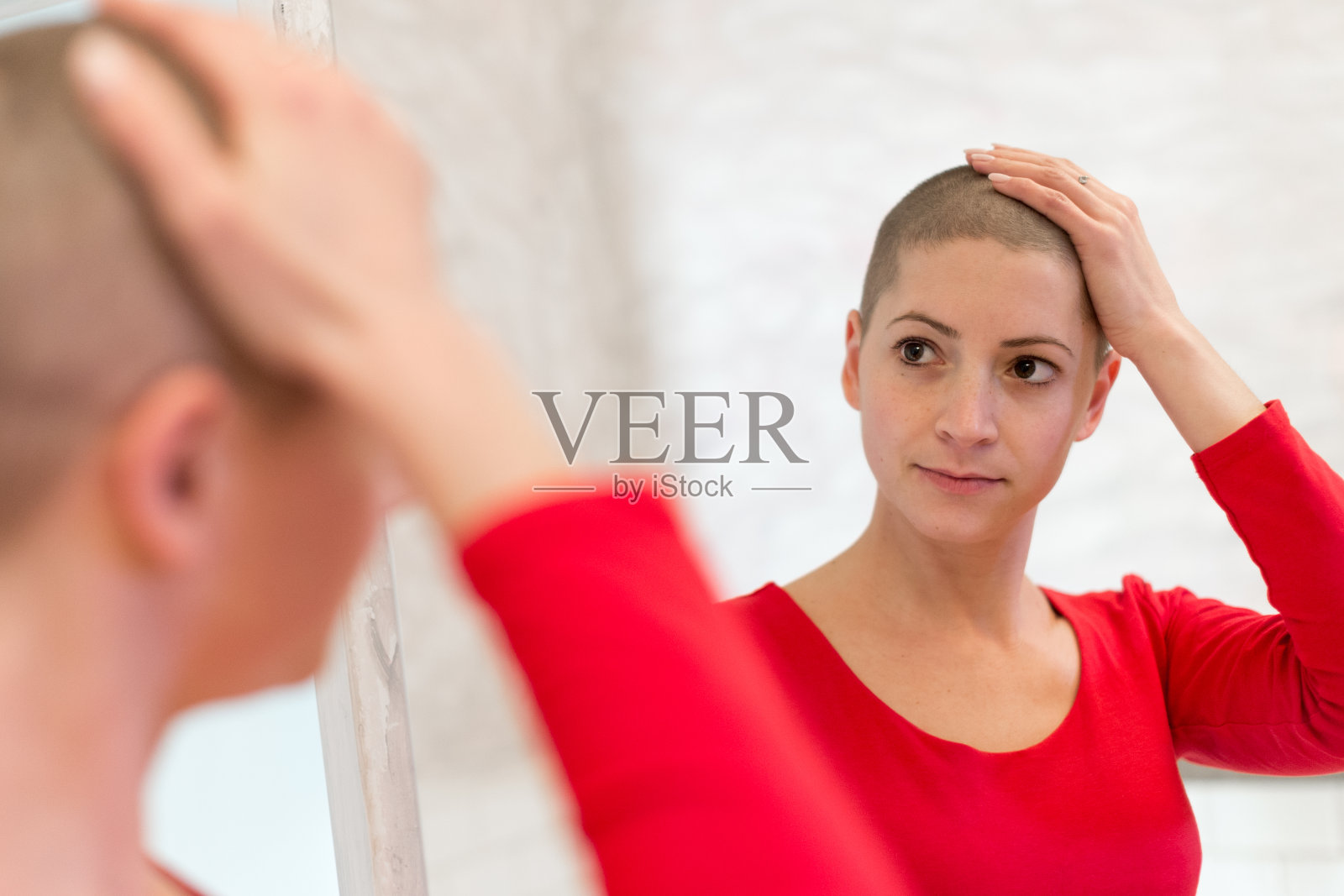 年轻的成年女性癌症患者看着镜子，抚摸着她的新短发。照片摄影图片