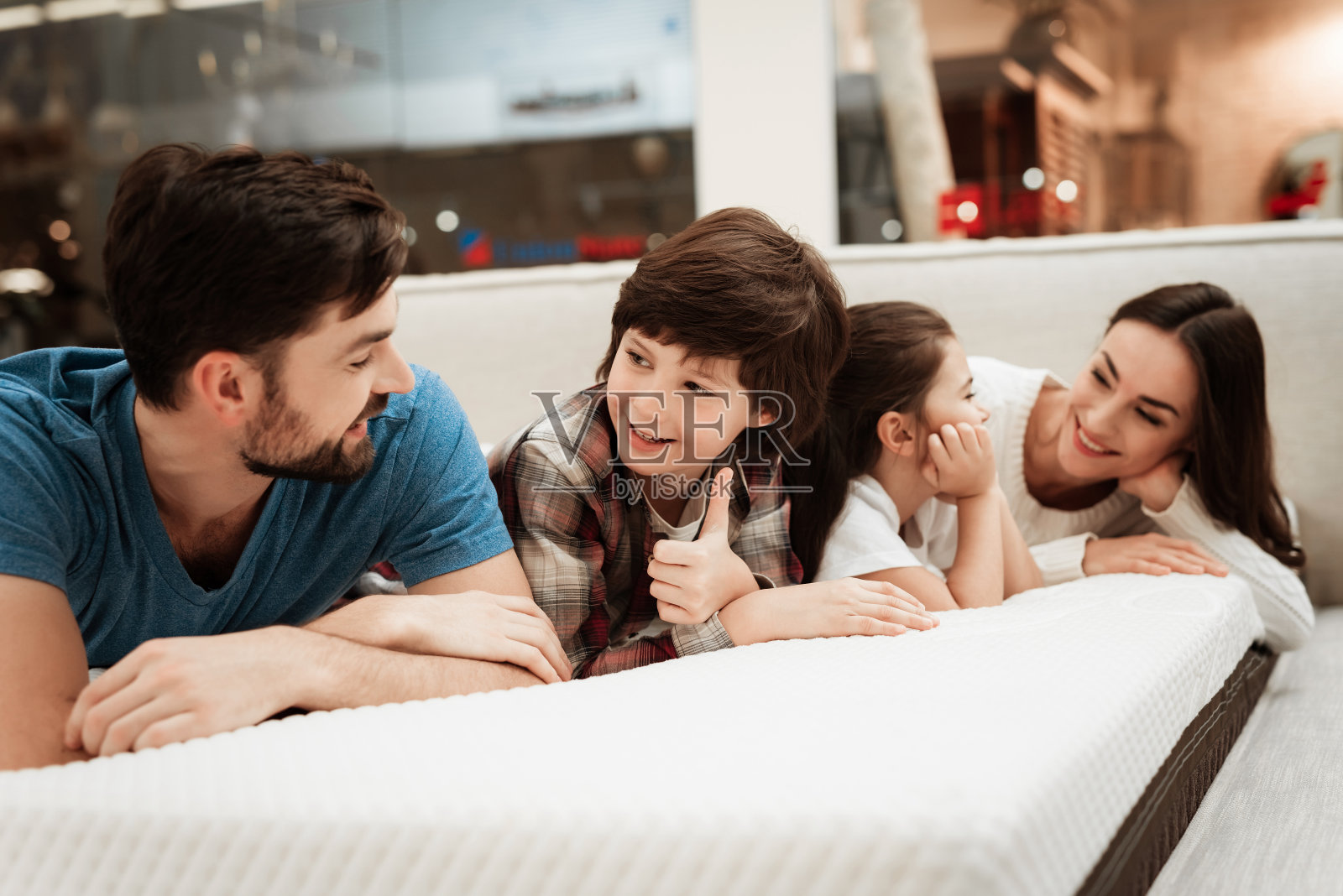 年轻幸福的家庭在家具店检查矫形床垫的柔软度，躺在床上。照片摄影图片