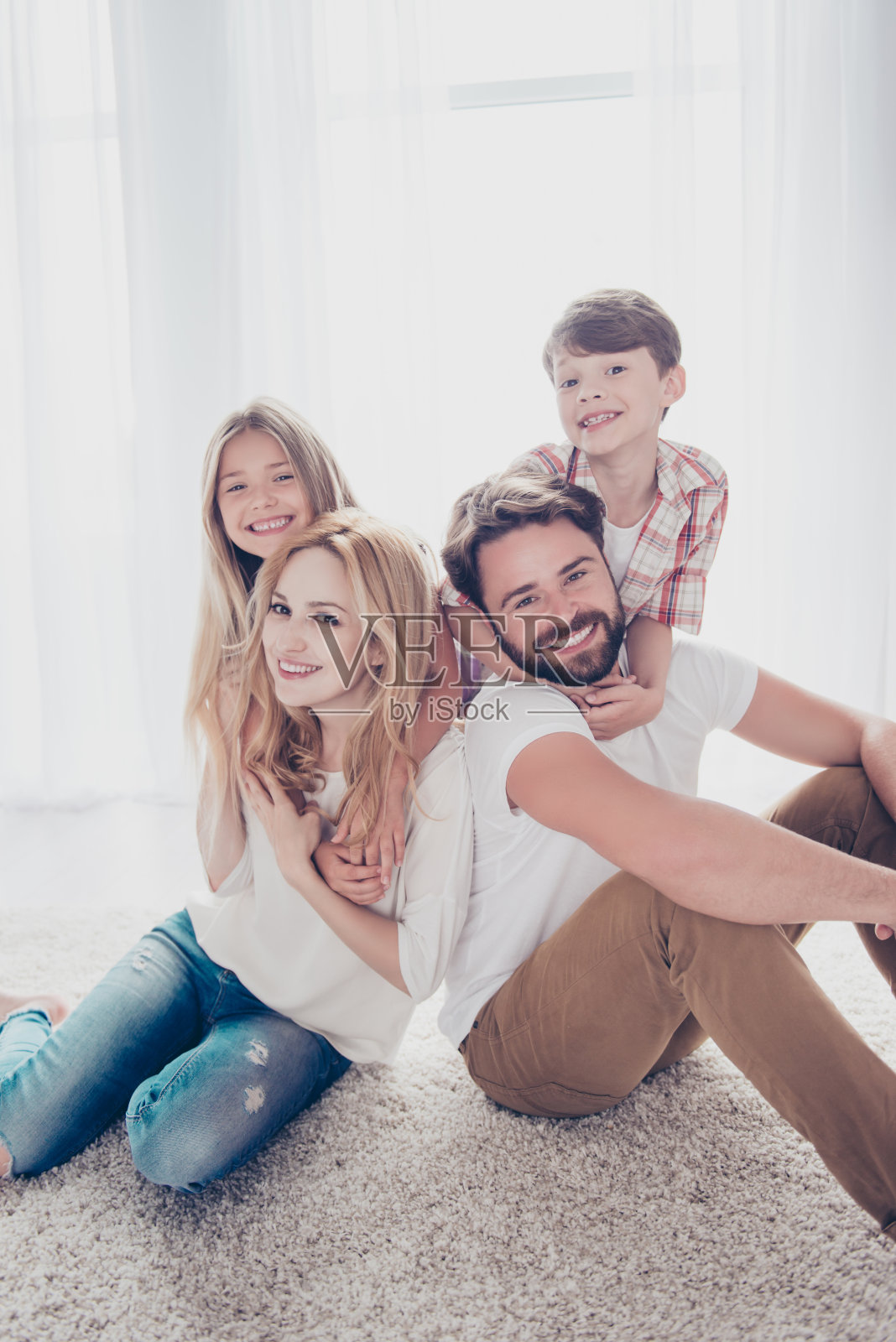 四人全家福。快乐的父母们在他们快乐的孩子们身后，金发的小女孩，黑发的男孩，坐在家里地板上的地毯上，个个面带微笑照片摄影图片