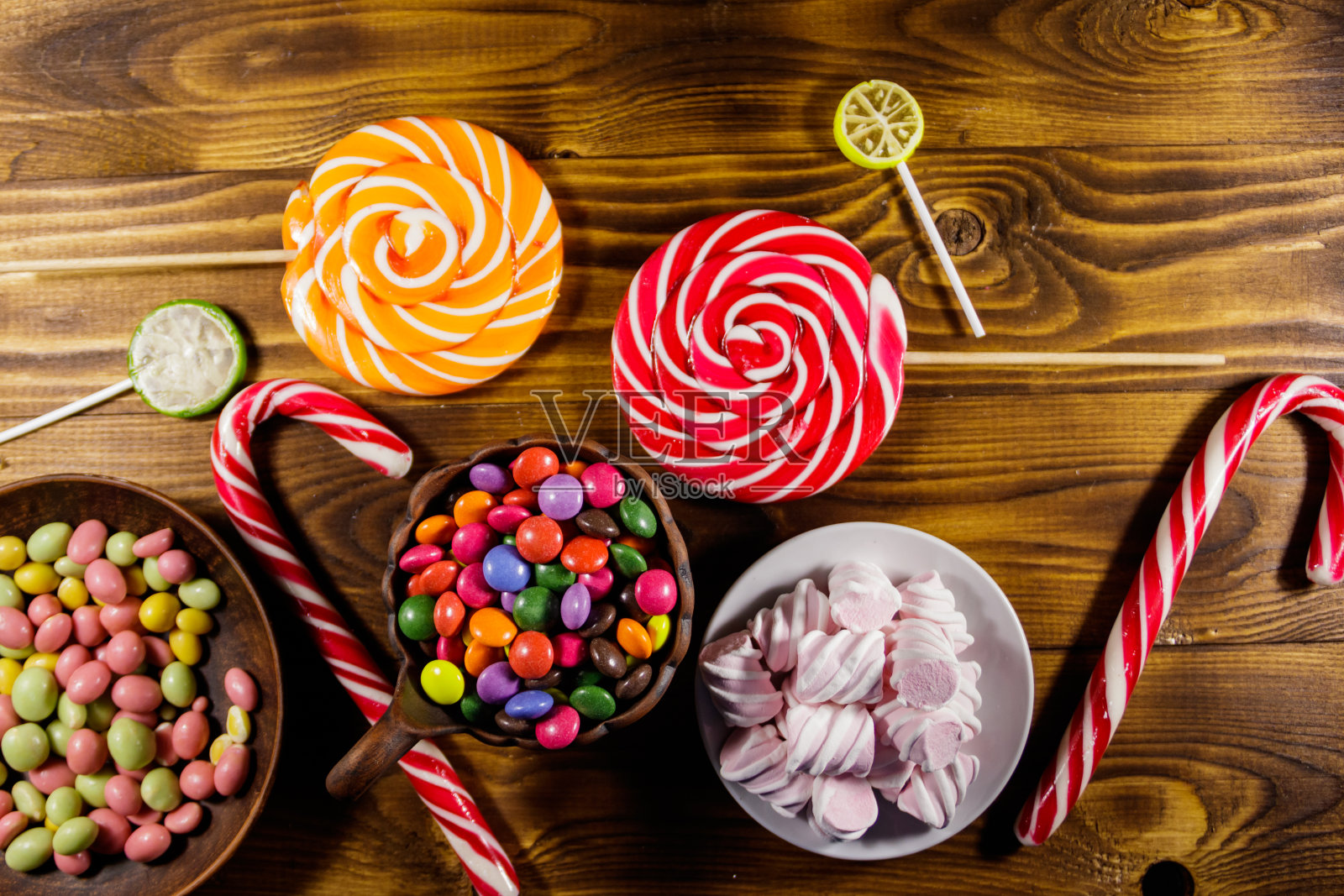 木桌上摆放着五颜六色的巧克力糖果、棒棒糖、甘蔗糖和棉花糖照片摄影图片