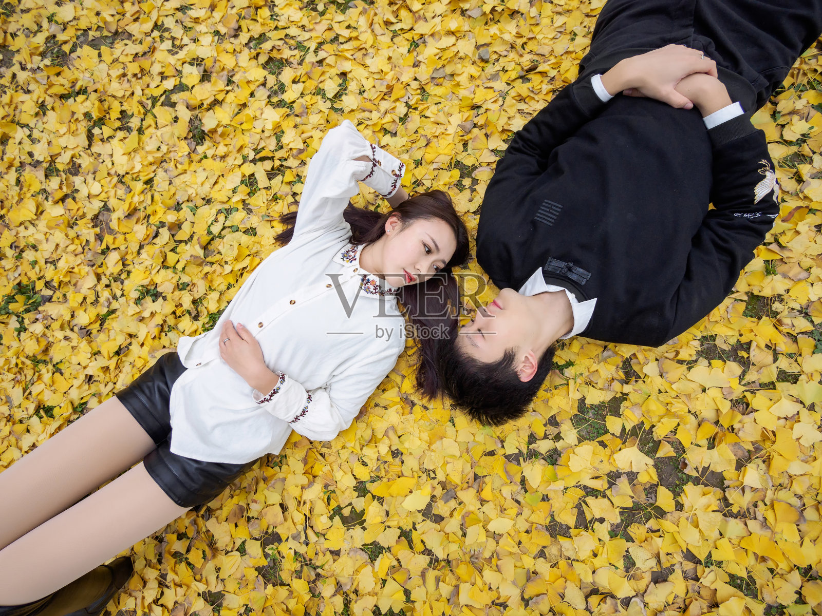 高角度观看一对中国年轻人躺在满是金黄银杏叶的秋日地面上，充满了爱情、情人的概念。照片摄影图片