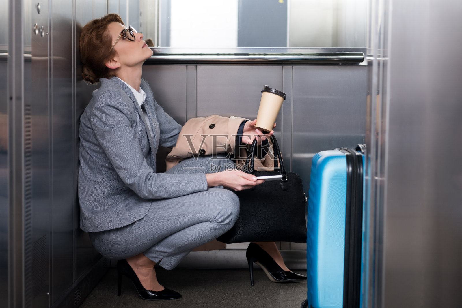 侧视图疲惫的女商人穿着智能手机和咖啡去电梯照片摄影图片