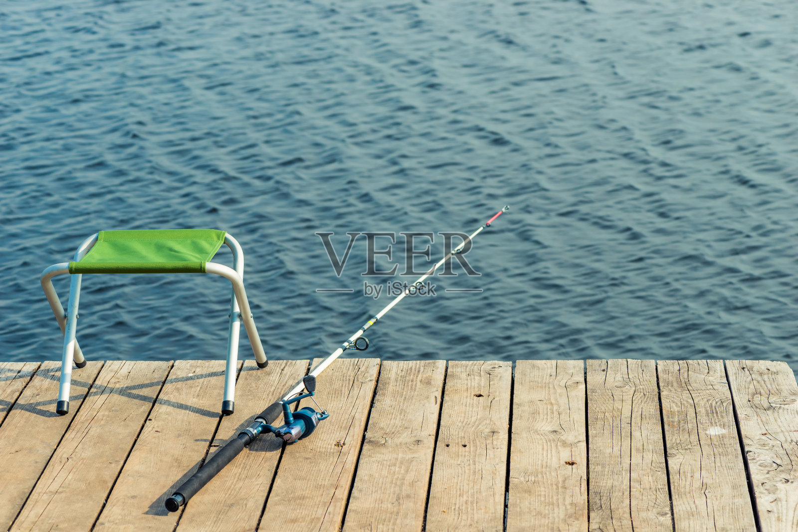 湖边的木码头上有一把空椅子和一根钓鱼竿照片摄影图片