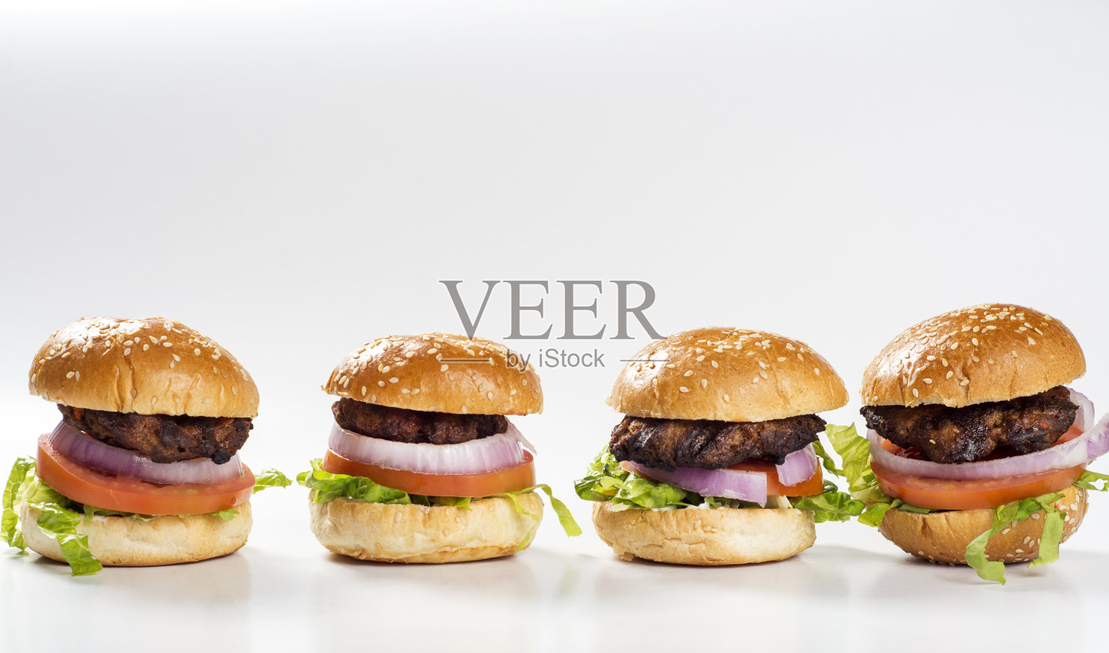 四个迷你汉堡一盘，有烤肉，洋葱片，番茄片，生菜叶和烤面包照片摄影图片