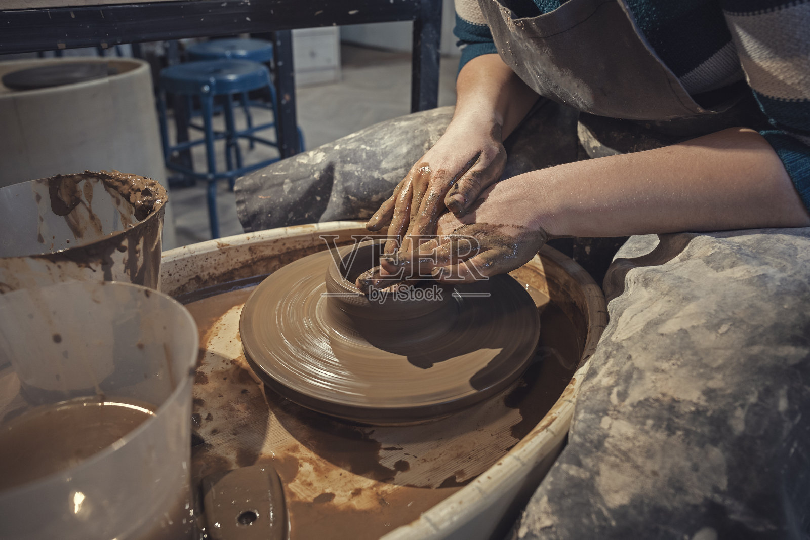 女工匠穿着围裙做陶器。工匠艺术家用他的手在陶轮上塑造罐子照片摄影图片
