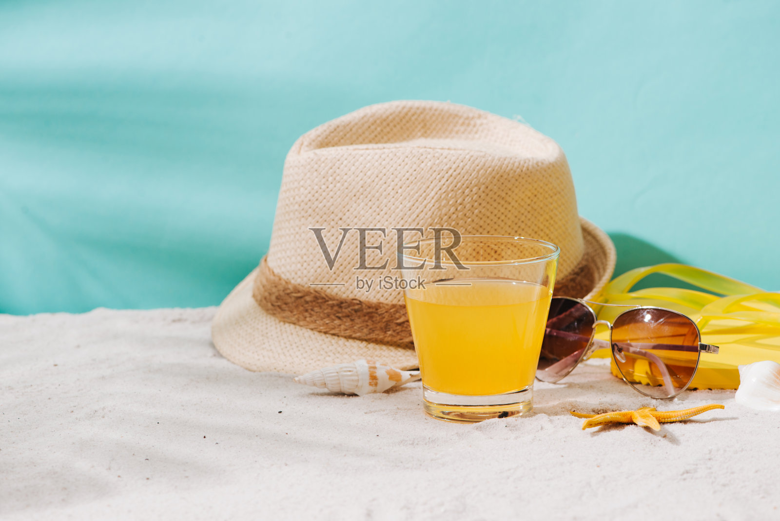 夏天的背景。沙滩配饰人字拖;太阳镜;帽子和橙汁上的沙子背景照片摄影图片