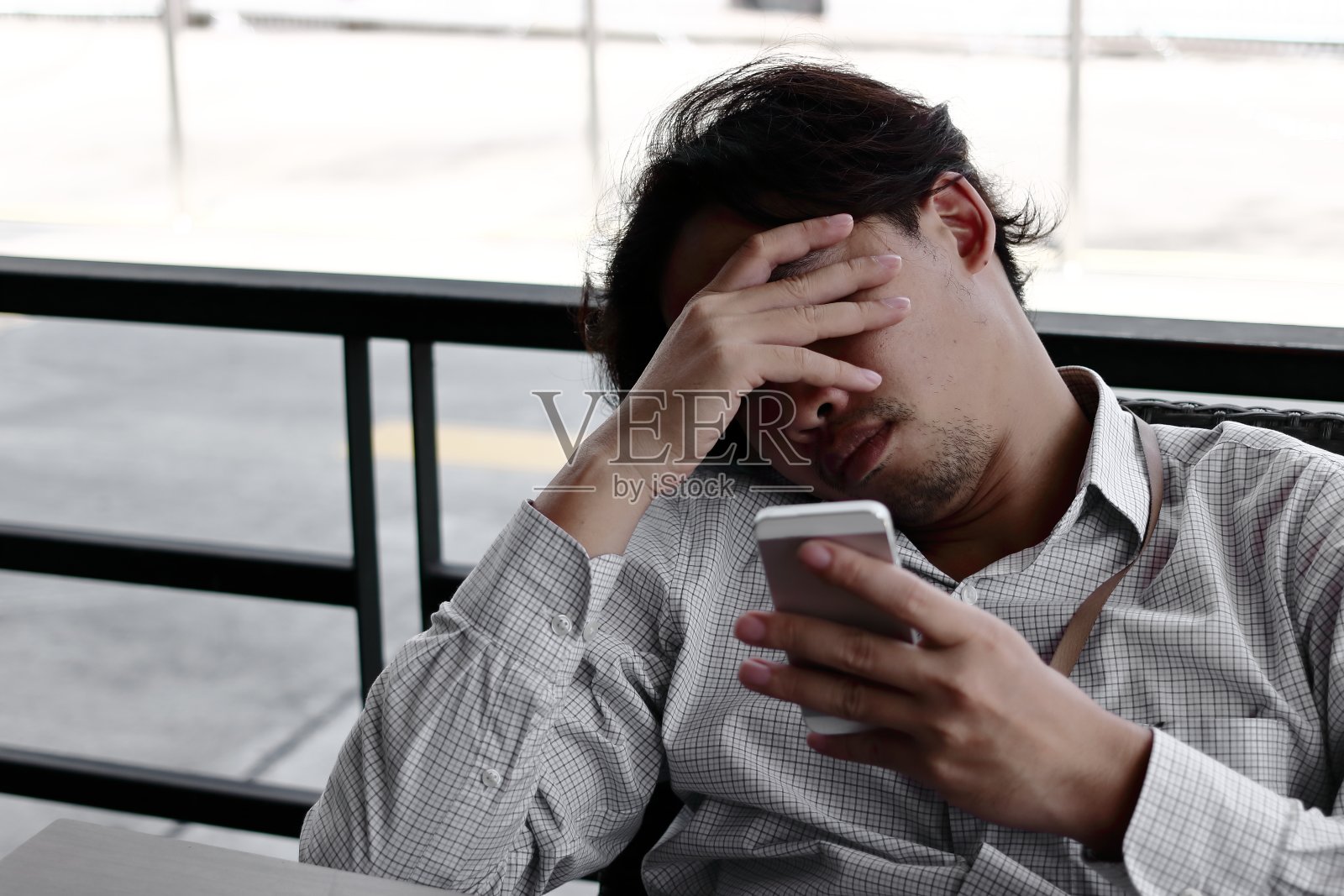 沮丧的亚洲商人与手在前额看移动智能手机在他的手在办公室。照片摄影图片