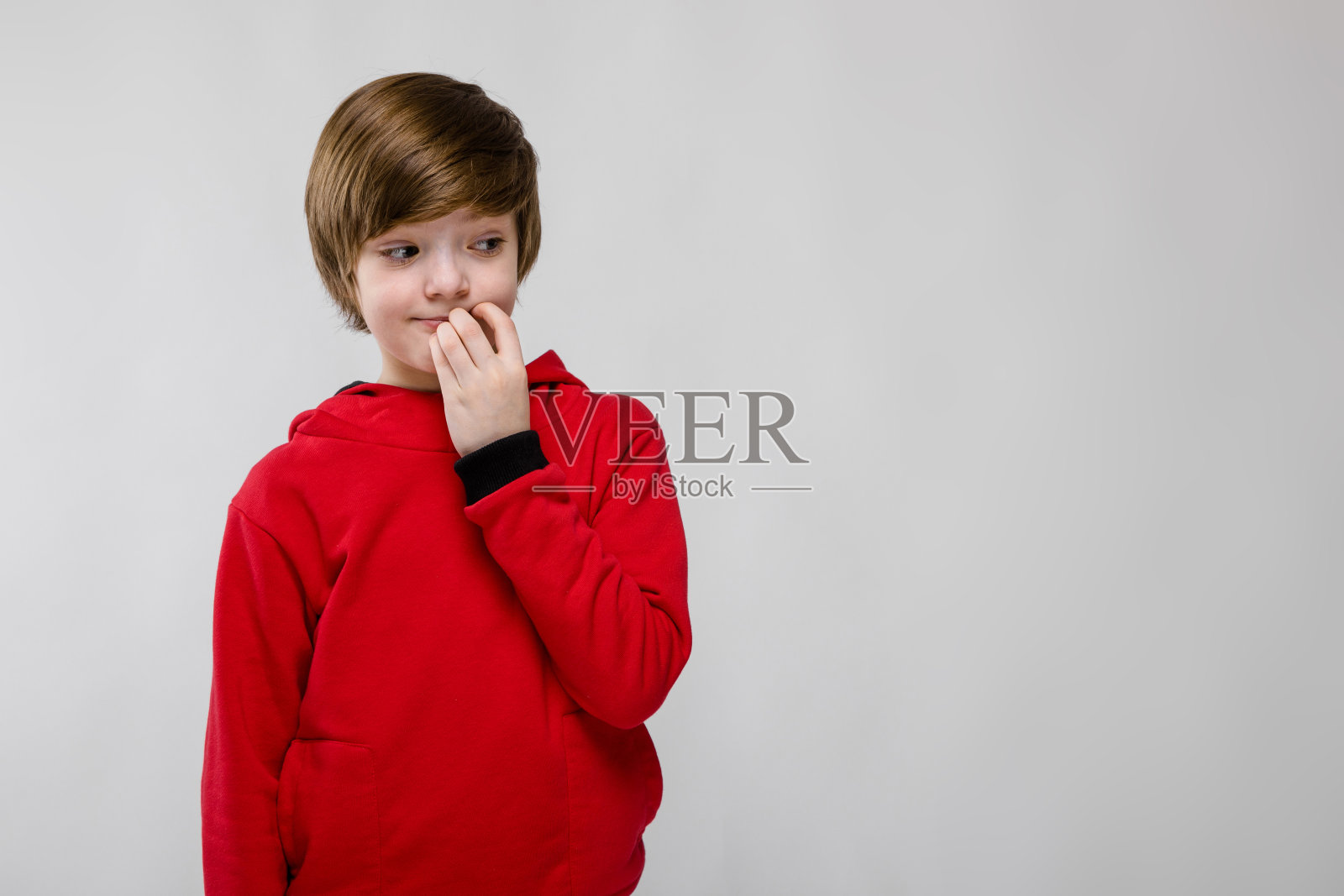 可爱自信的小白人男孩在红色毛衣思考与手靠近他的脸在灰色的背景照片摄影图片