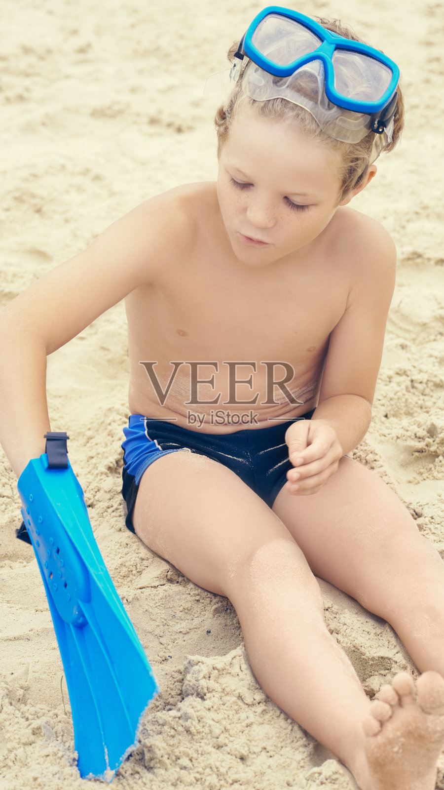 带着浮潜设备的白人小男孩坐在热带海滩的沙滩上。照片摄影图片