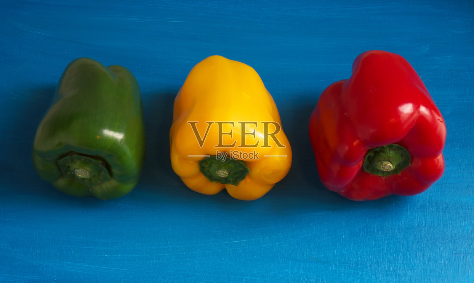 三个不同颜色的辣椒孤立在蓝色背景上照片摄影图片