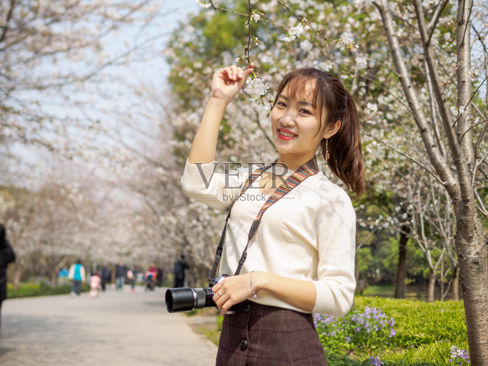 户外肖像美丽的年轻中国女孩微笑在盛开的樱桃树早午餐与相机挂在脖子在春天的花园，美丽，夏天，情感，表达和人们的概念。照片摄影图片