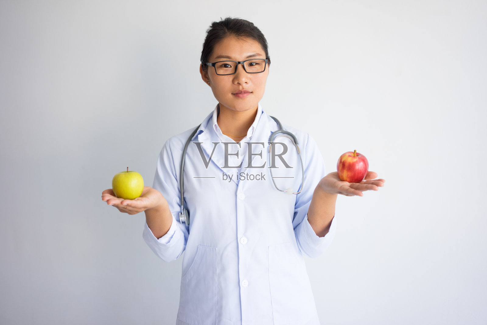 严肃的年轻亚洲女医生拿着红和黄的苹果照片摄影图片