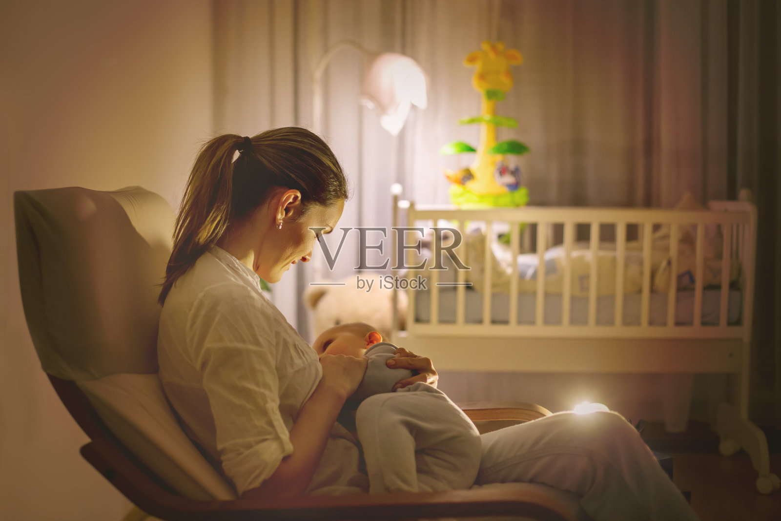 年轻美丽的母亲，在昏暗的灯光下给她的新生儿喂奶照片摄影图片_ID:317217189-Veer图库