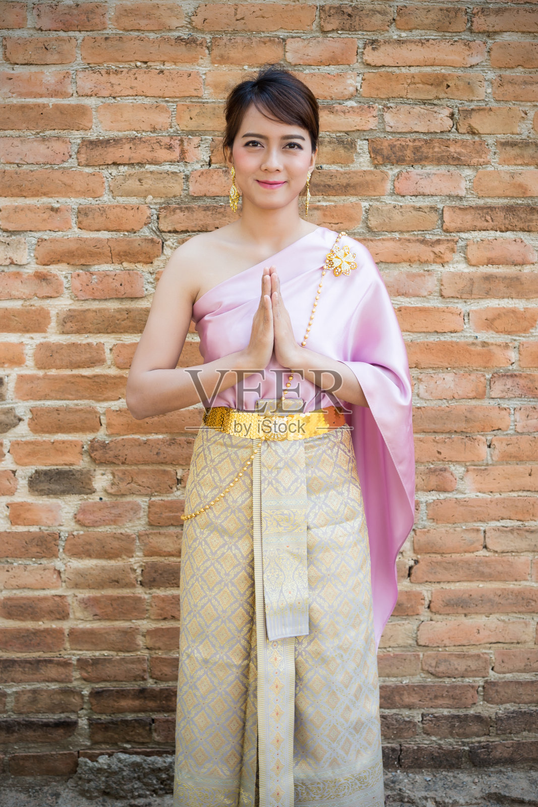 妇女站在那里，穿着泰国传统服装或以古代墙壁为背景的泰国服饰。欢迎或你好照片摄影图片