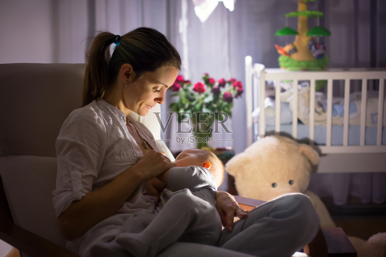 年轻美丽的母亲，在昏暗的灯光下给她的新生儿喂奶照片摄影图片