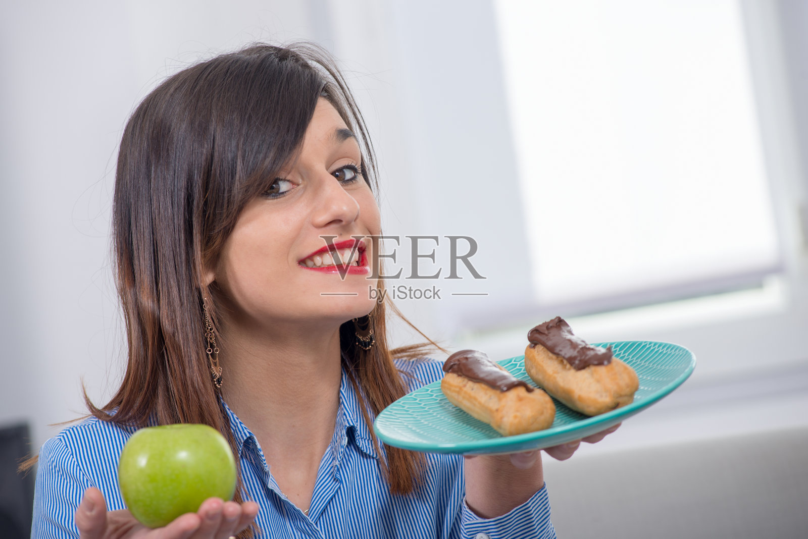 年轻女子在苹果和巧克力糕点之间做出选择照片摄影图片
