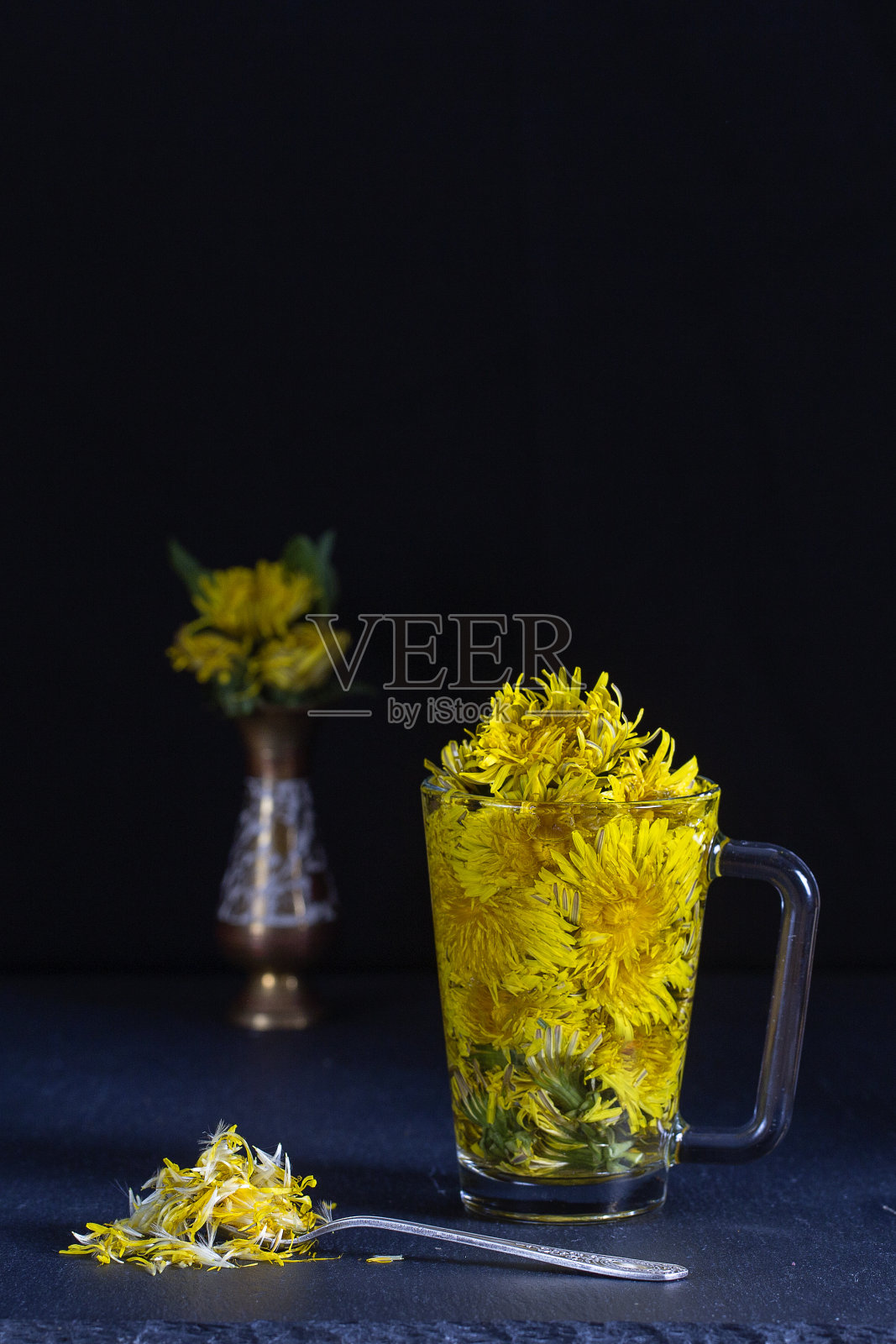 蒲公英黄花茶饮在玻璃杯上的黑色背景。健康饮食的概念照片摄影图片