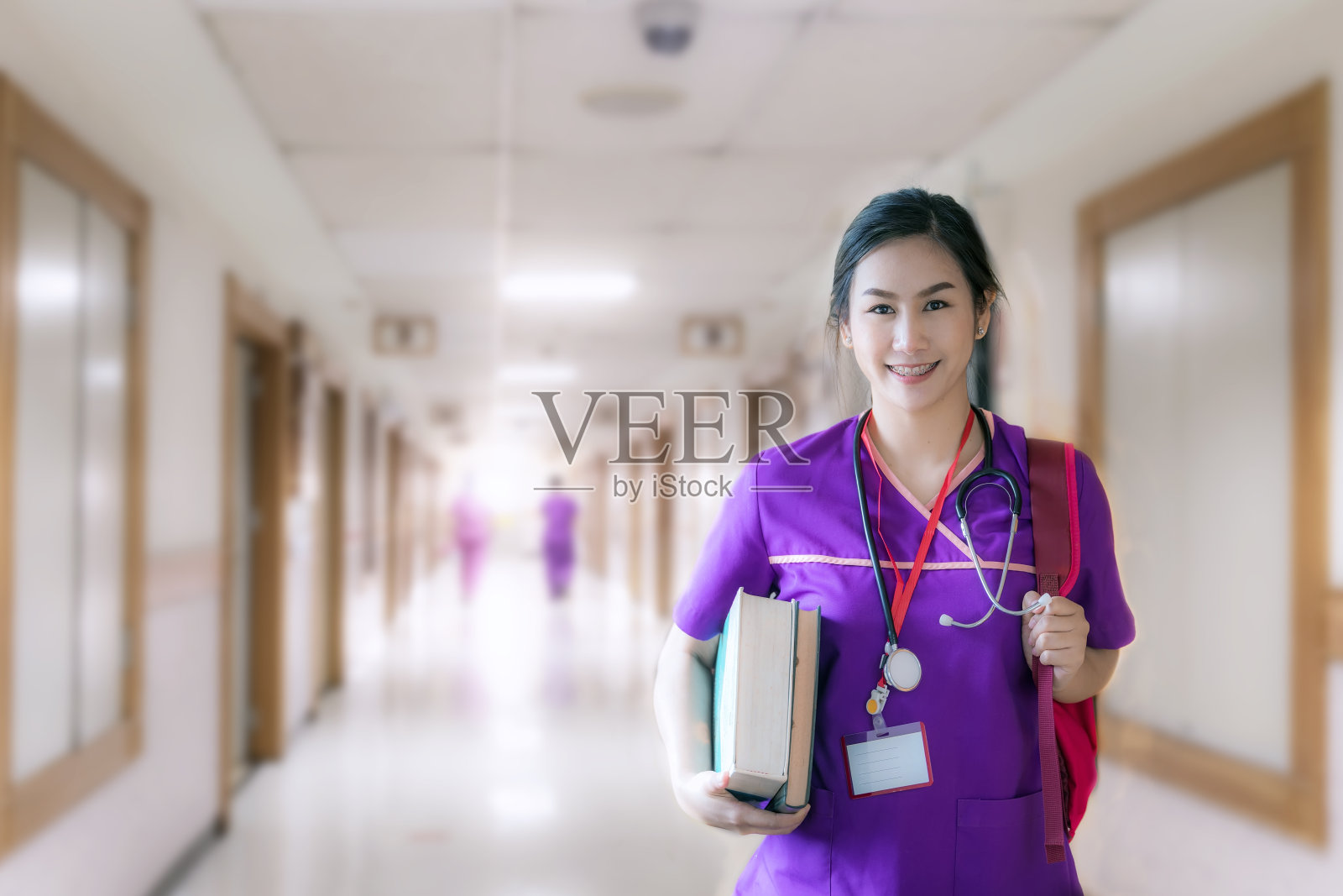 身穿紫色制服，背着背包的护士站着，拿着书照片摄影图片