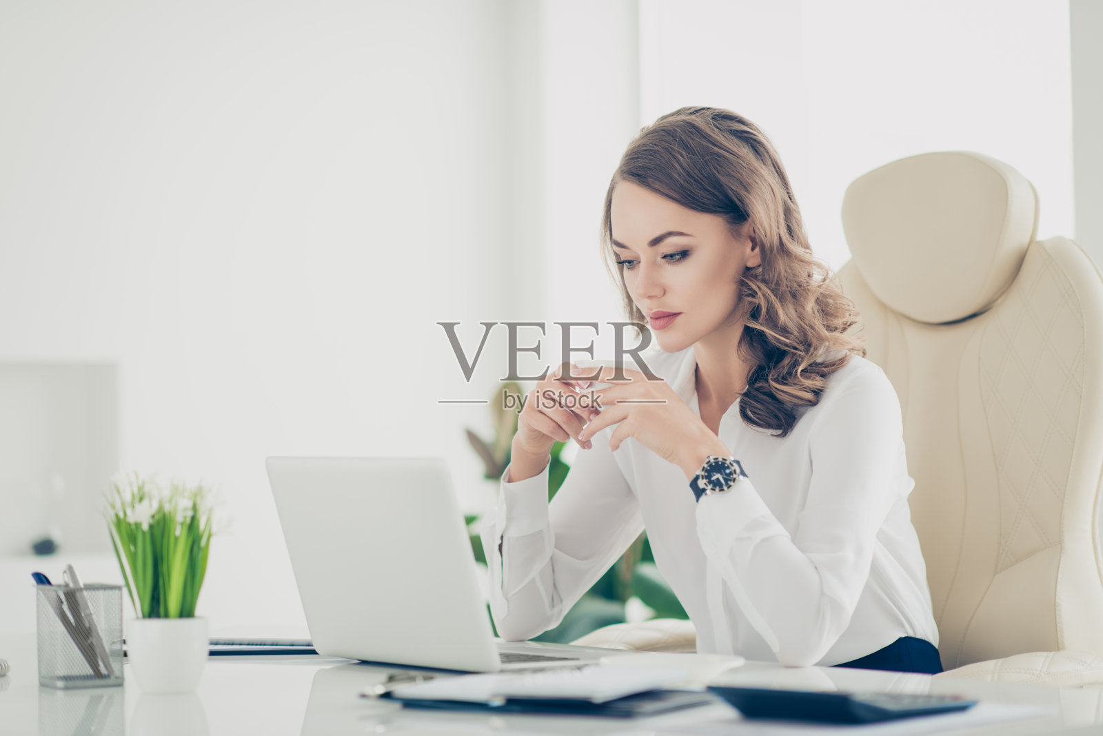 肖像时尚，时尚，迷人，漂亮，漂亮的女人与现代发型在白衬衫看着笔记本电脑的屏幕，手里拿着一杯茶坐在工作地点的工作站看电影视频照片摄影图片