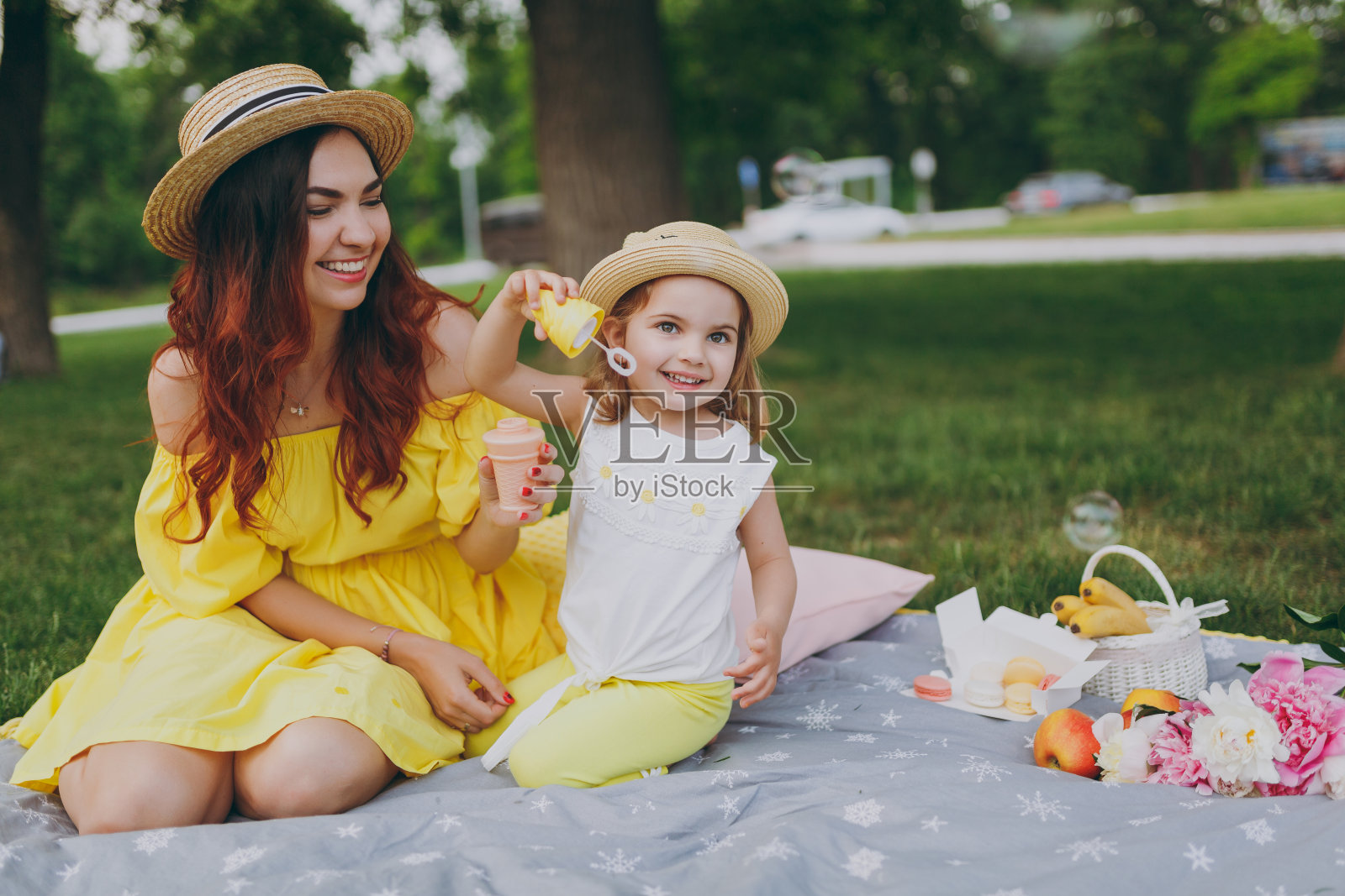 身着黄色连衣裙的微笑女子在公园的绿色草地上玩耍，与可爱的小宝贝宝贝女孩抱着肥皂泡吹风机休息。妈妈，小女儿。母亲节，爱家庭，为人父母，童年。照片摄影图片
