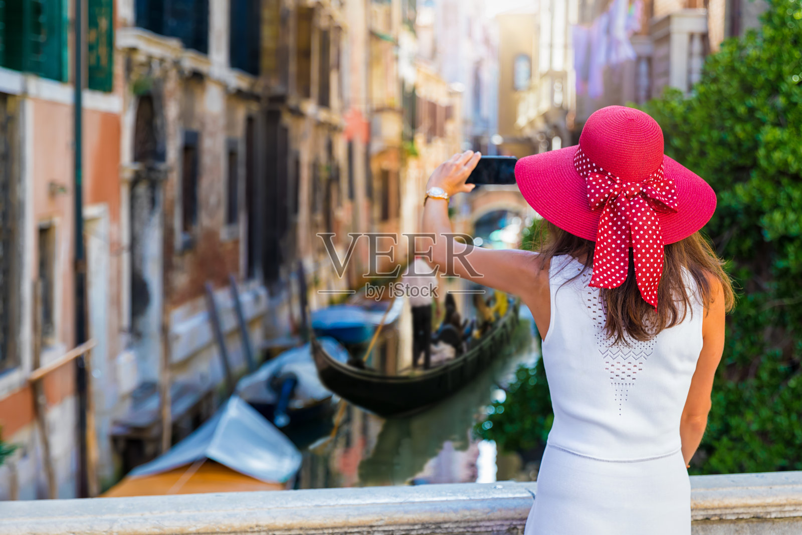一位戴着红色太阳帽的妇女在威尼斯的小运河上拍照照片摄影图片