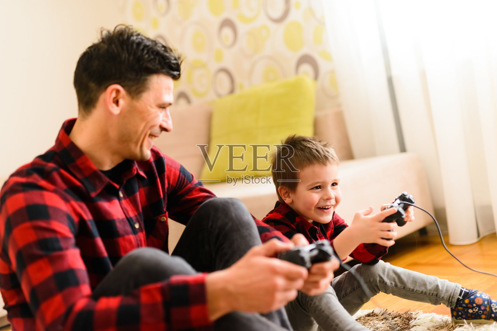 快乐的父子俩坐在地板上玩电子游戏。他们俩都很兴奋。照片摄影图片
