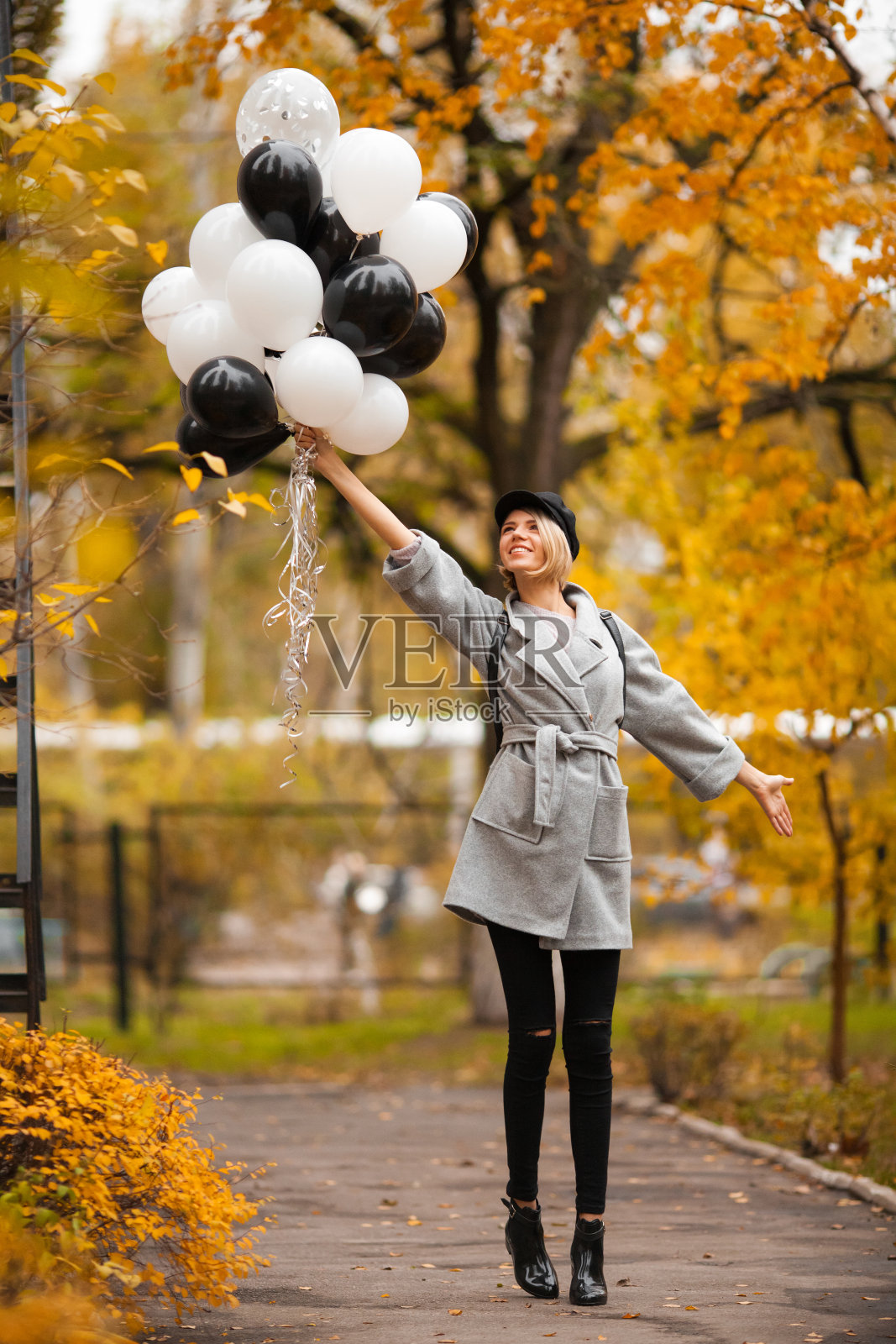 秋天的女人在秋天的公园里拿着气球。穿着灰色外套的时尚女孩照片摄影图片