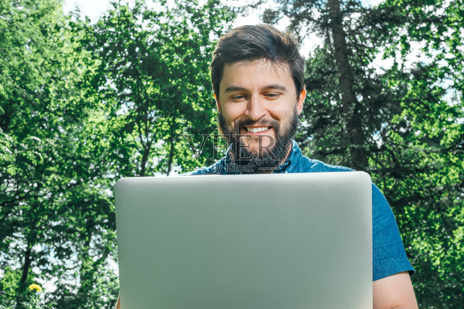 一个快乐的嬉皮士，带着笔记本电脑坐在户外的绿草地上。自由的概念照片摄影图片