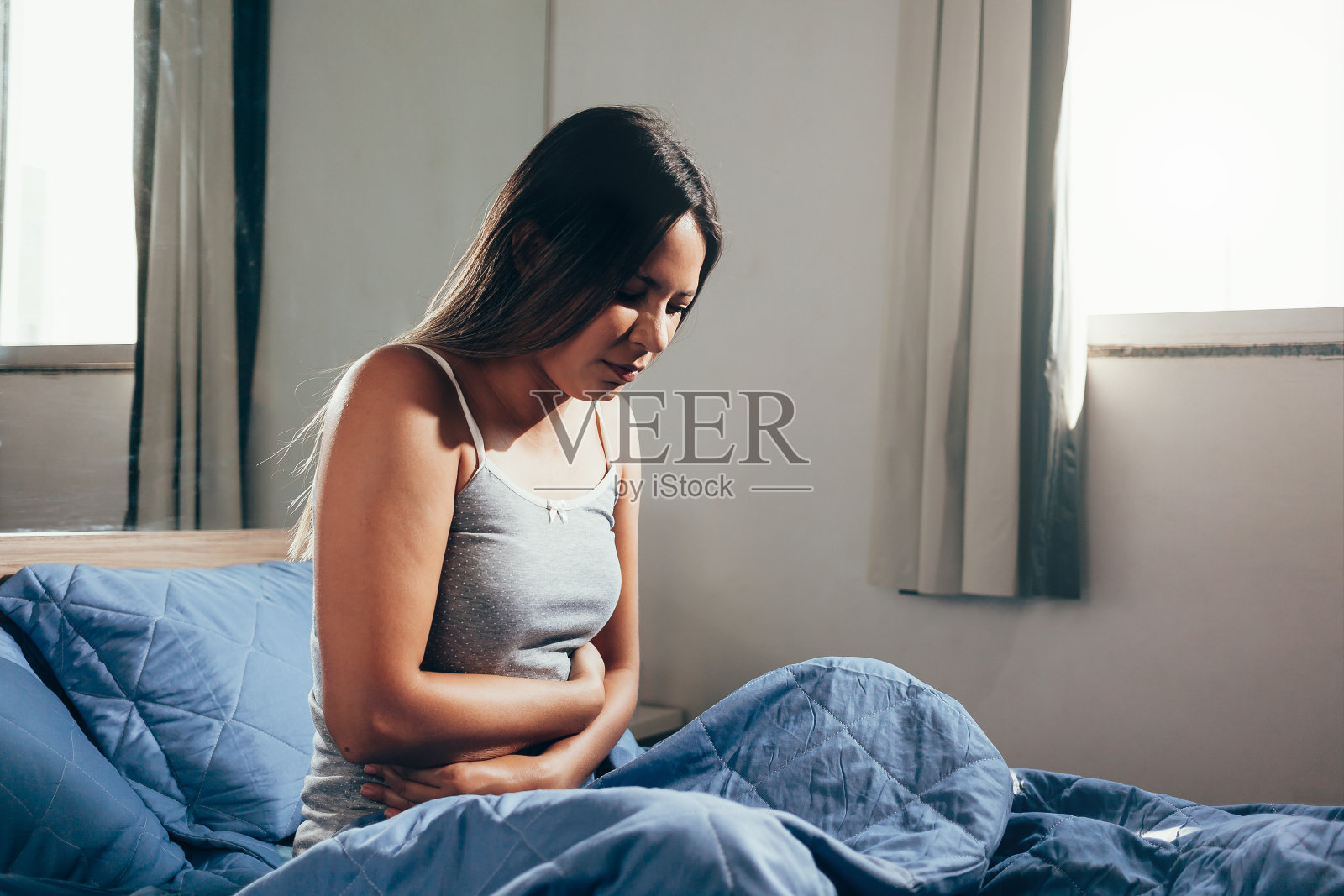 年轻女子在睡衣抓她的肚子，而痛苦的胃痛在她的床上照片摄影图片