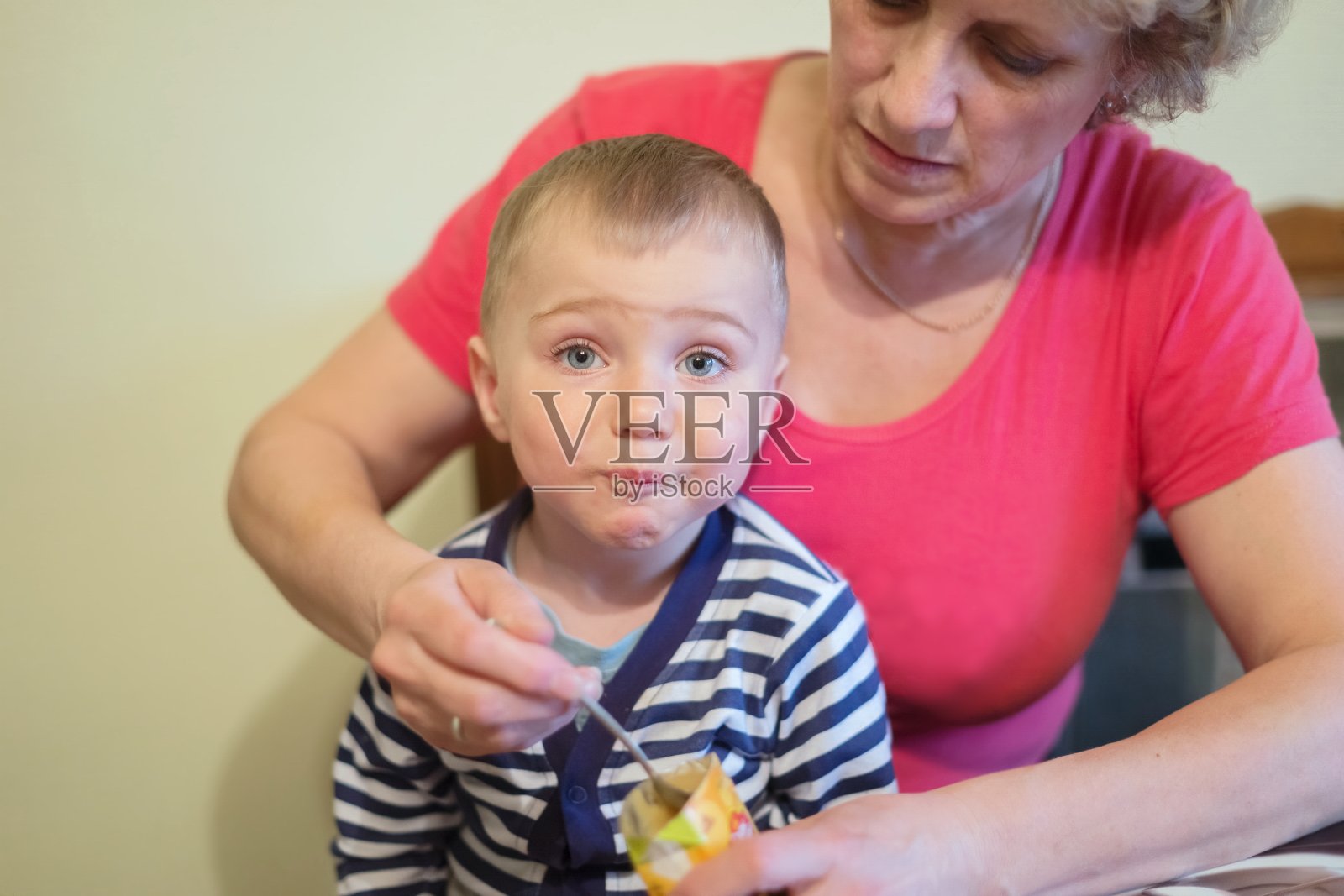 妇女在家里用勺子喂一个1.5岁的小男孩。照片摄影图片