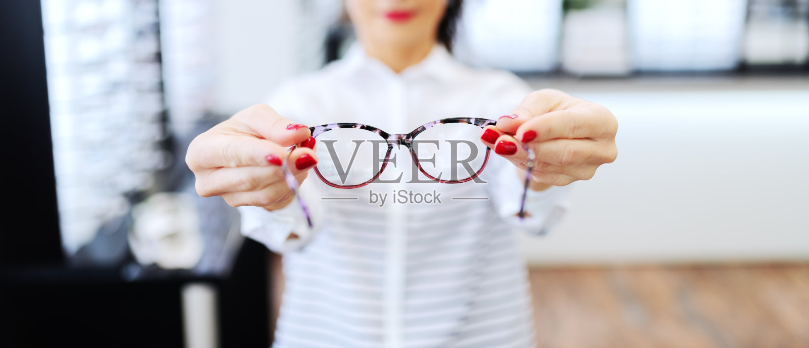 一个女人在眼镜店拿着她想买的眼镜。选择性地关注眼镜。照片摄影图片