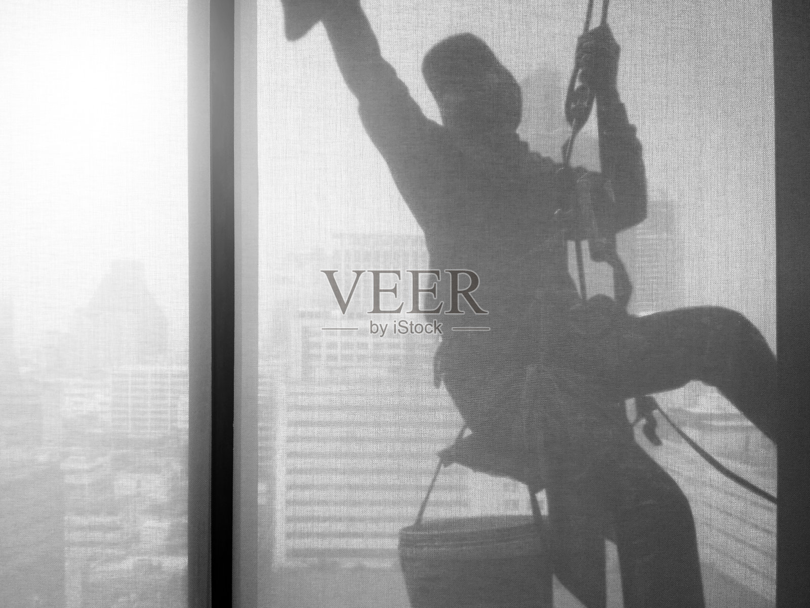 一名男子在高层办公楼的窗户上清洗，透过建筑内部的透明窗帘效果拍摄剪影图像照片摄影图片