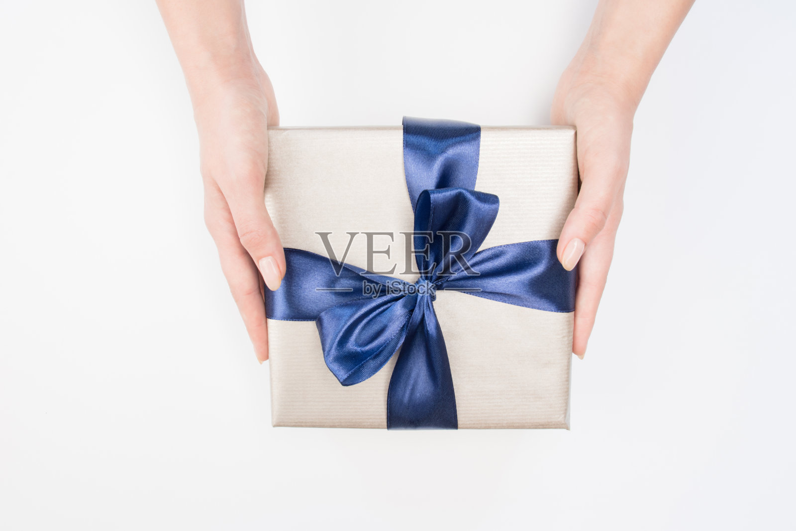 一个孤立的背景上，女人的手拿着深蓝色蝴蝶结的礼物盒。节日的概念。照片摄影图片