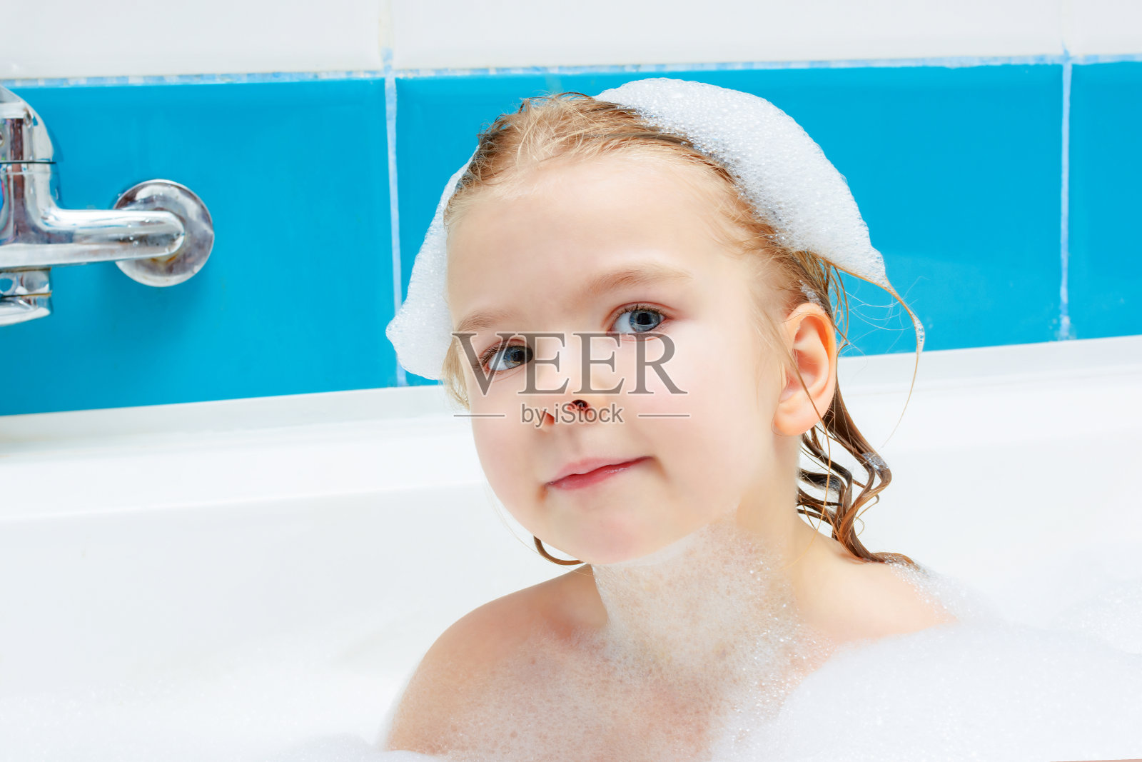 小女孩正在洗澡。满面笑容，头上沾着泡沫的孩子。光照片。照片摄影图片