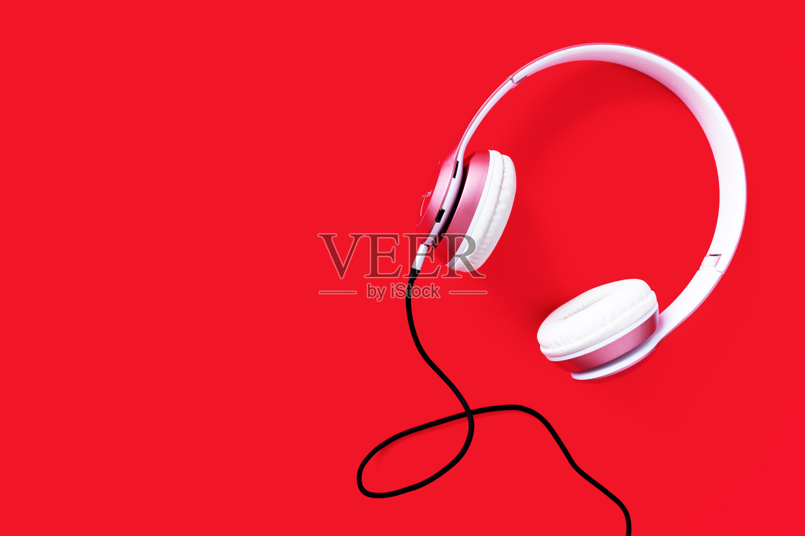 粉色耳机和黑色电缆在柔和的颜色红色背景。音乐的概念。空白空间复制照片摄影图片