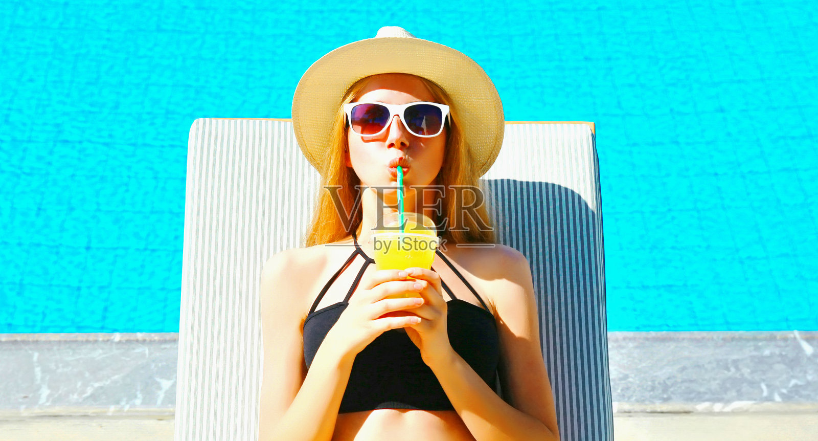 暑假-肖像女人喝果汁在躺椅上蓝色的水池背景照片摄影图片